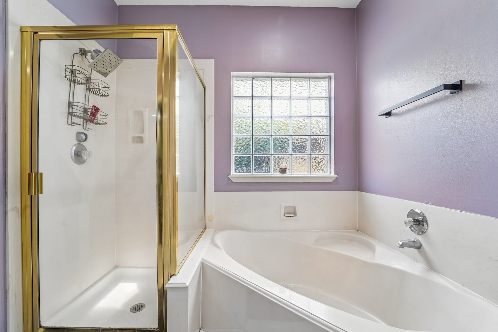 Charming bathroom features a spacious soaking tub and a separate glass-enclosed shower, complemented by elegant purple walls and a window for natural light.