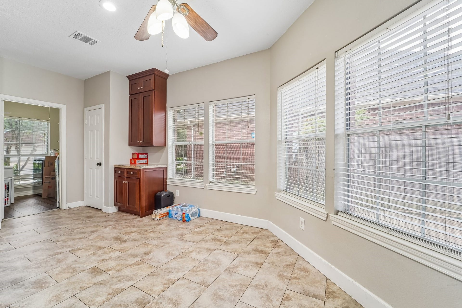 Bright and airy room with large windows, tiled flooring, and a ceiling fan, ideal for a sunlit dining area or cozy sitting space.