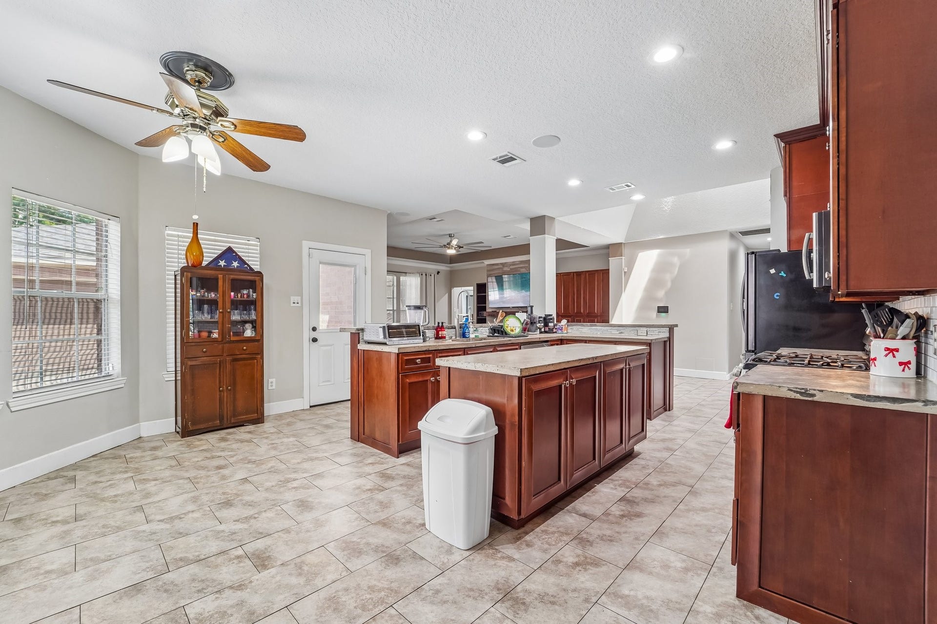 Spacious kitchen featuring rich wood cabinetry, a large central island, and modern appliances, complemented by tile flooring and ample natural light.