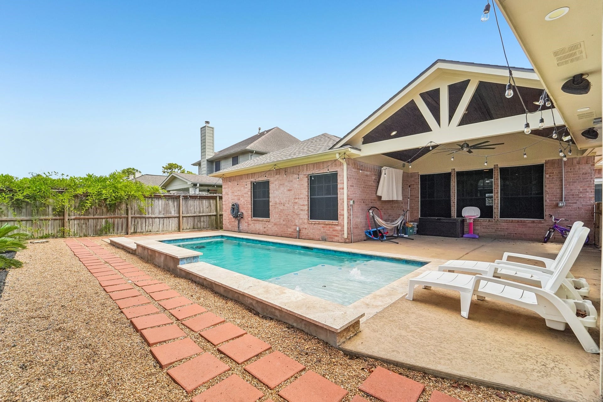 Charming backyard oasis featuring a sparkling pool, spacious patio, and cozy seating area, perfect for relaxing and entertaining.