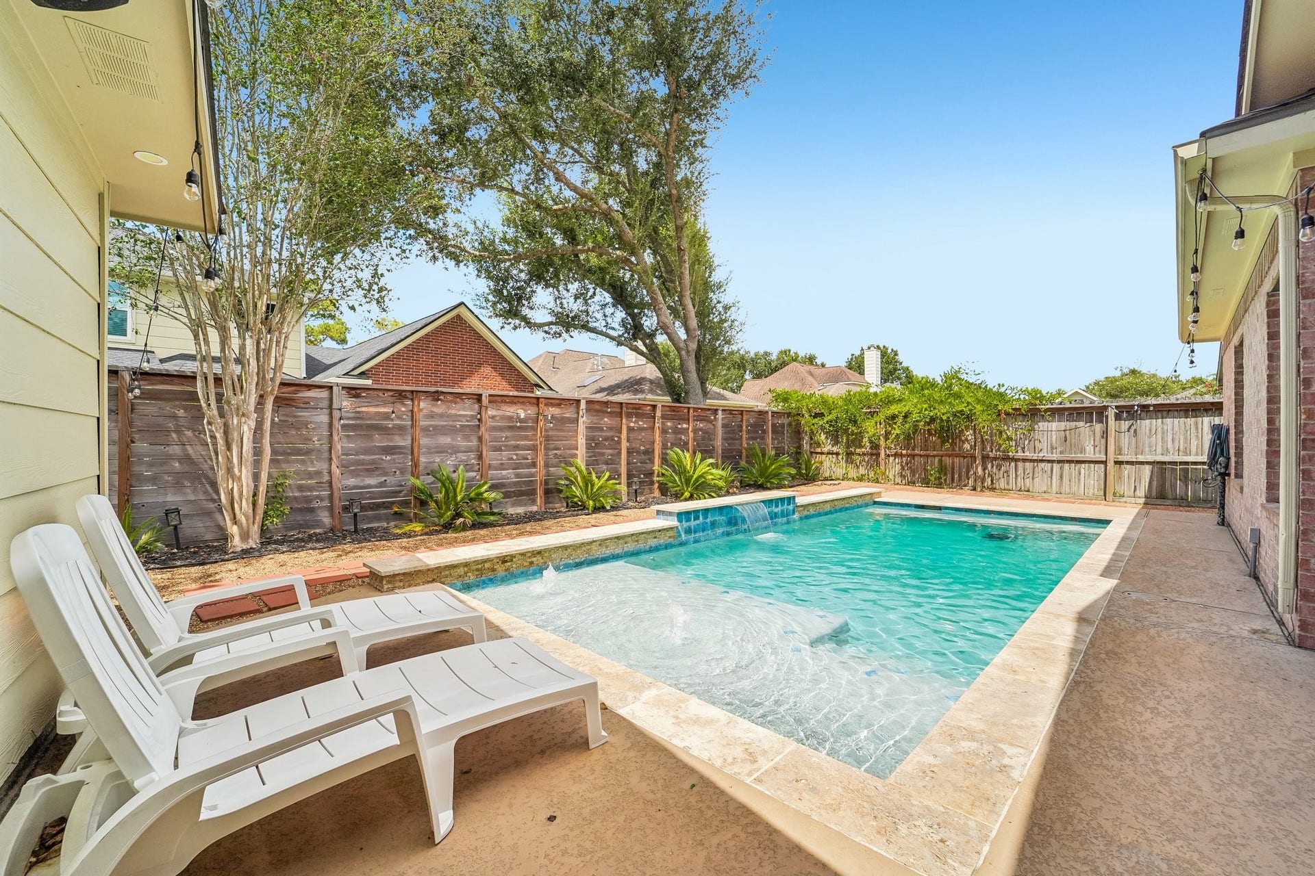 Enjoy a serene backyard oasis featuring a sparkling pool surrounded by lush greenery and ample space for relaxation on the sunlit deck.