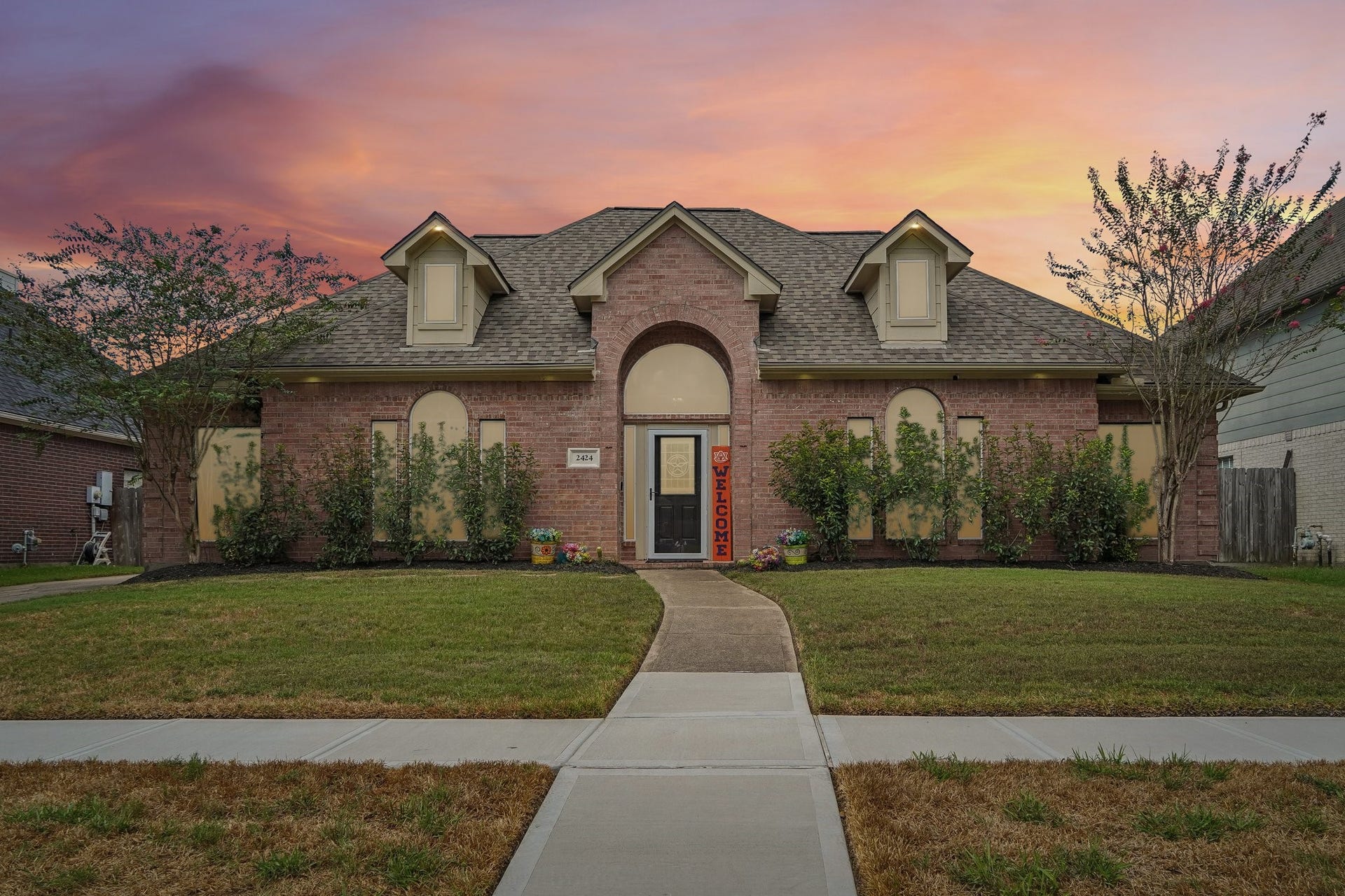 Charming brick home with a welcoming archway entrance, surrounded by manicured landscaping and set against a stunning sunset backdrop.