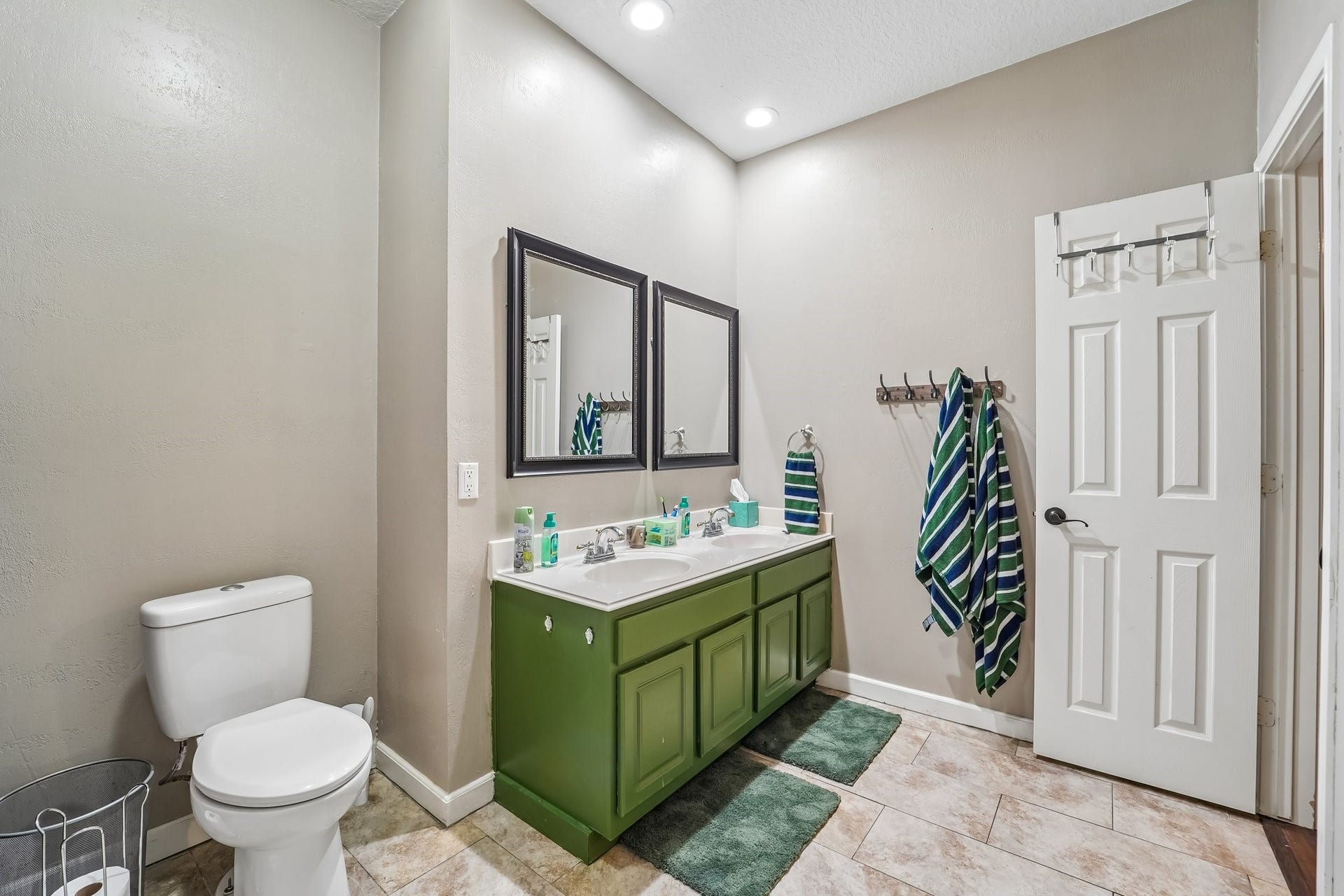 Modern bathroom featuring a dual-sink vanity with vibrant green cabinetry, complemented by stylish mirrors and ample lighting.