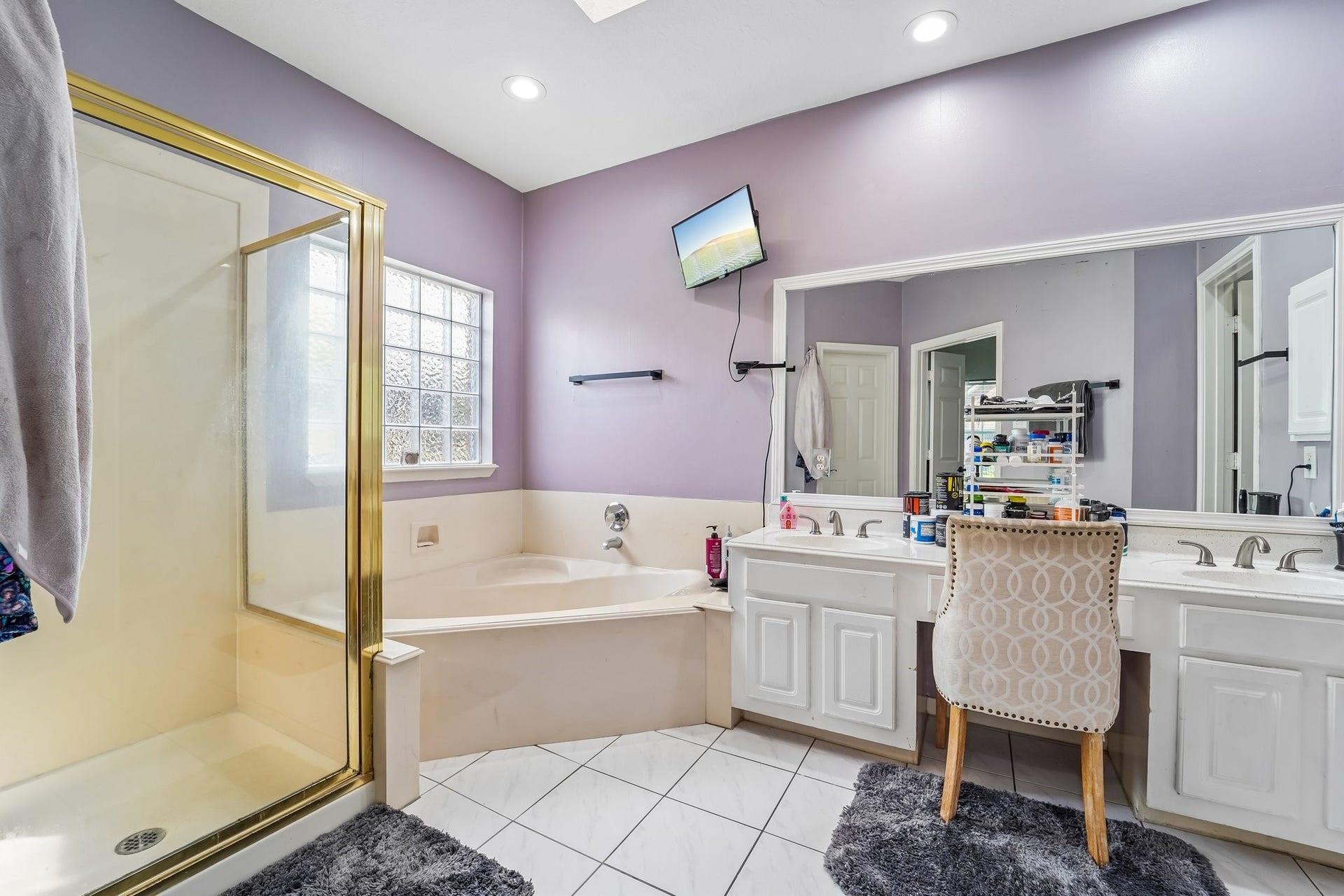 Elegant bathroom featuring a luxurious corner tub, separate shower with gold accents, and dual vanities with ample storage and a large mirror.