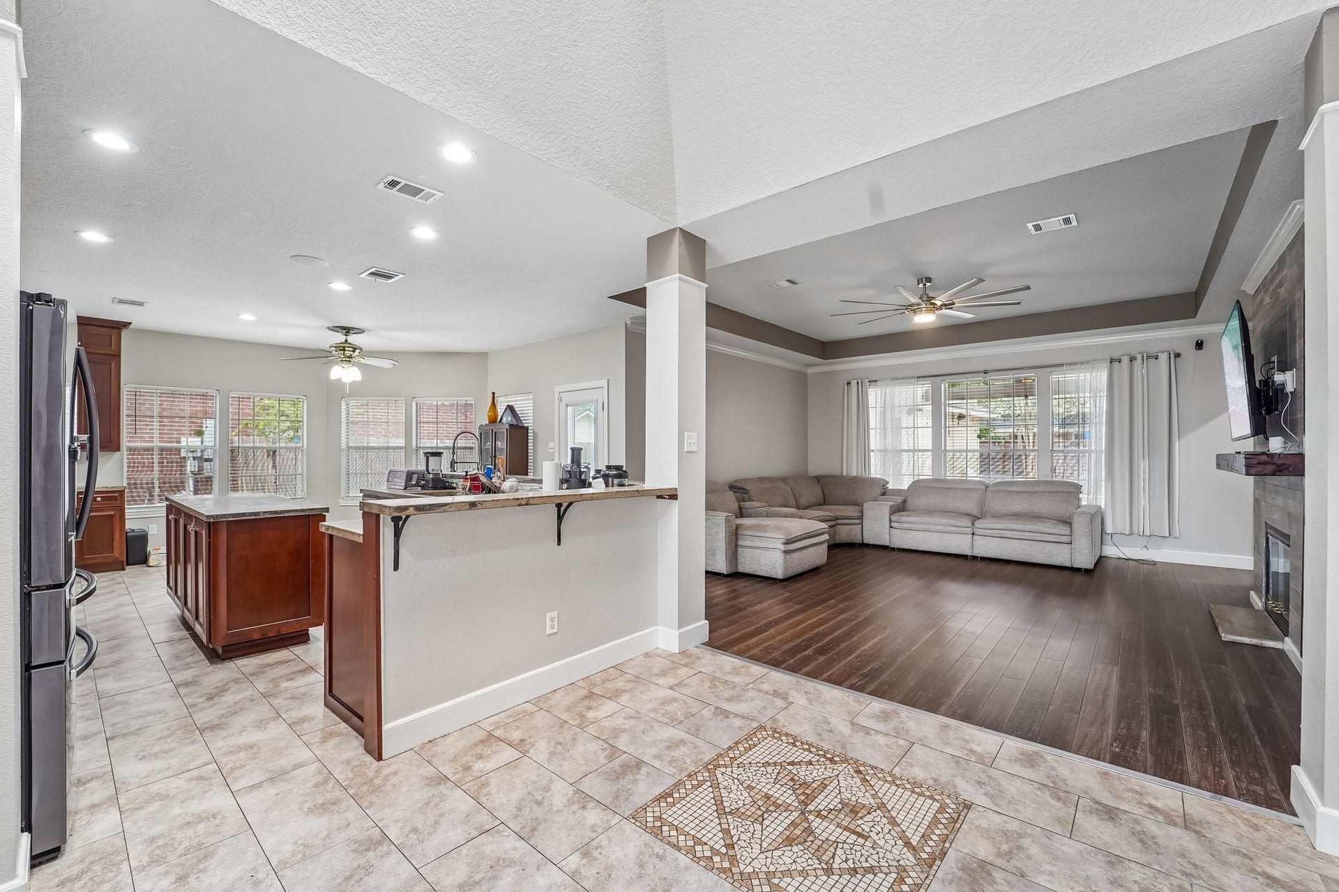Open-concept living area featuring a spacious kitchen with an island, tiled flooring, and an inviting living room with hardwood floors and a cozy fireplace.