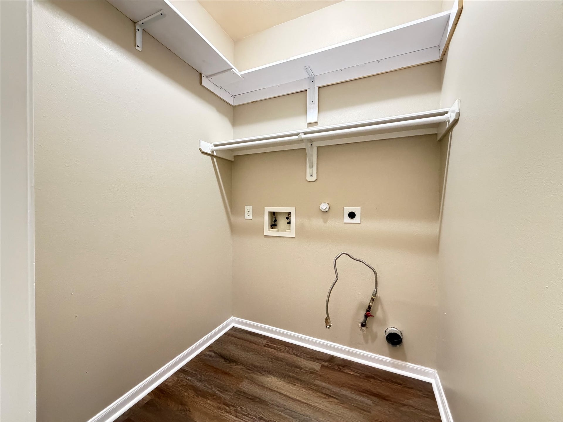 Convenient laundry area with washer/dryer hookups, shelving, and wood-look flooring for a neat and functional space, inside the house.