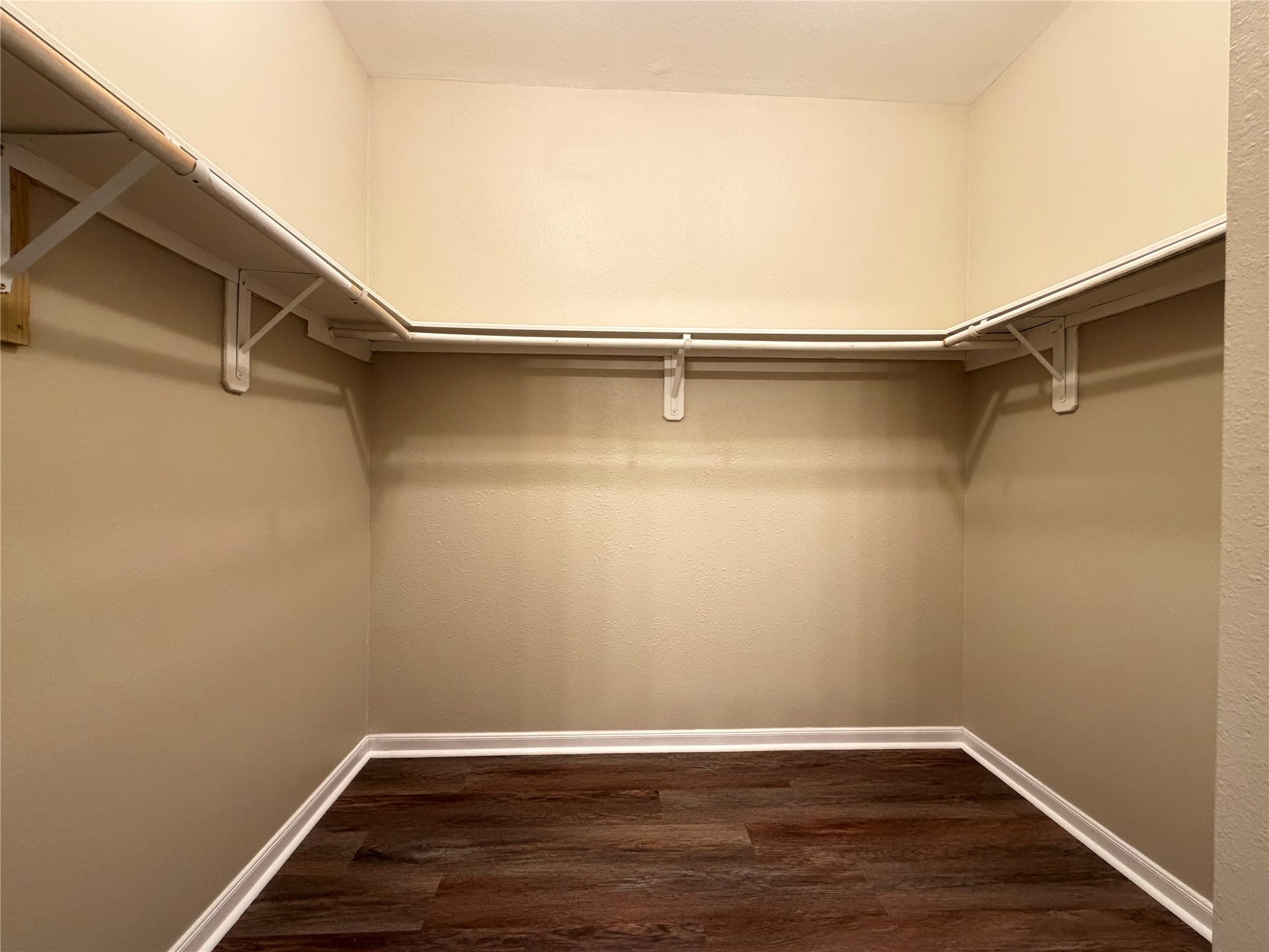 Spacious primary walk-in closet with ample shelving and rich, dark wood-like flooring.