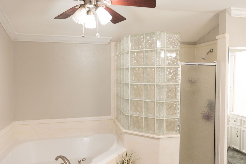 1314 Laurel Street, La Marque, TX 77568 Bright bathroom with a corner glass block shower, a large soaking tub, neutral walls, and a ceiling fan. Ideal for a relaxing retreat.