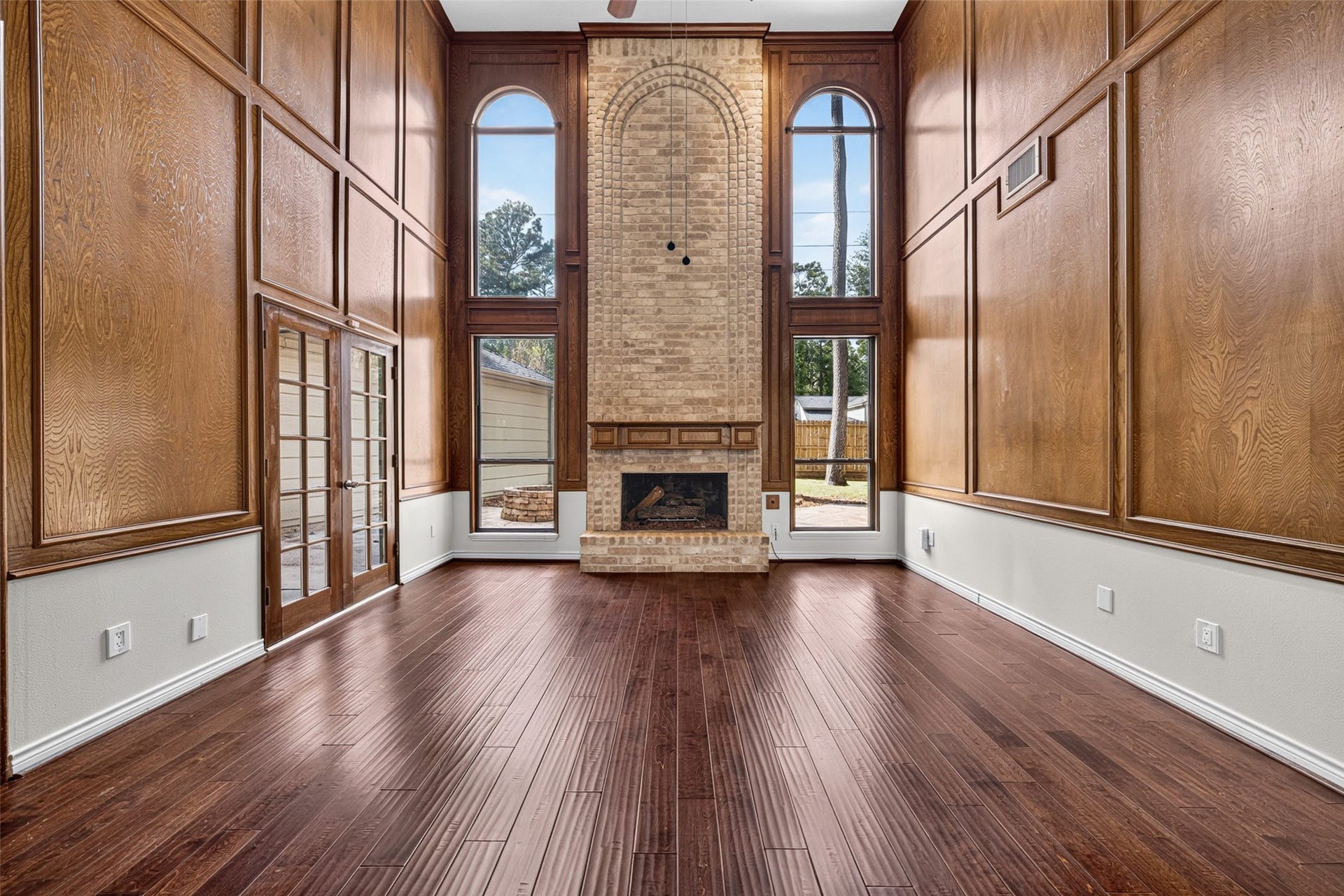 6206 Willow Pine Drive, Spring, TX 77379 Stunning living room with soaring ceilings, rich wood paneling, and an elegant brick fireplace, accented by tall arched windows that flood the space with natural light.