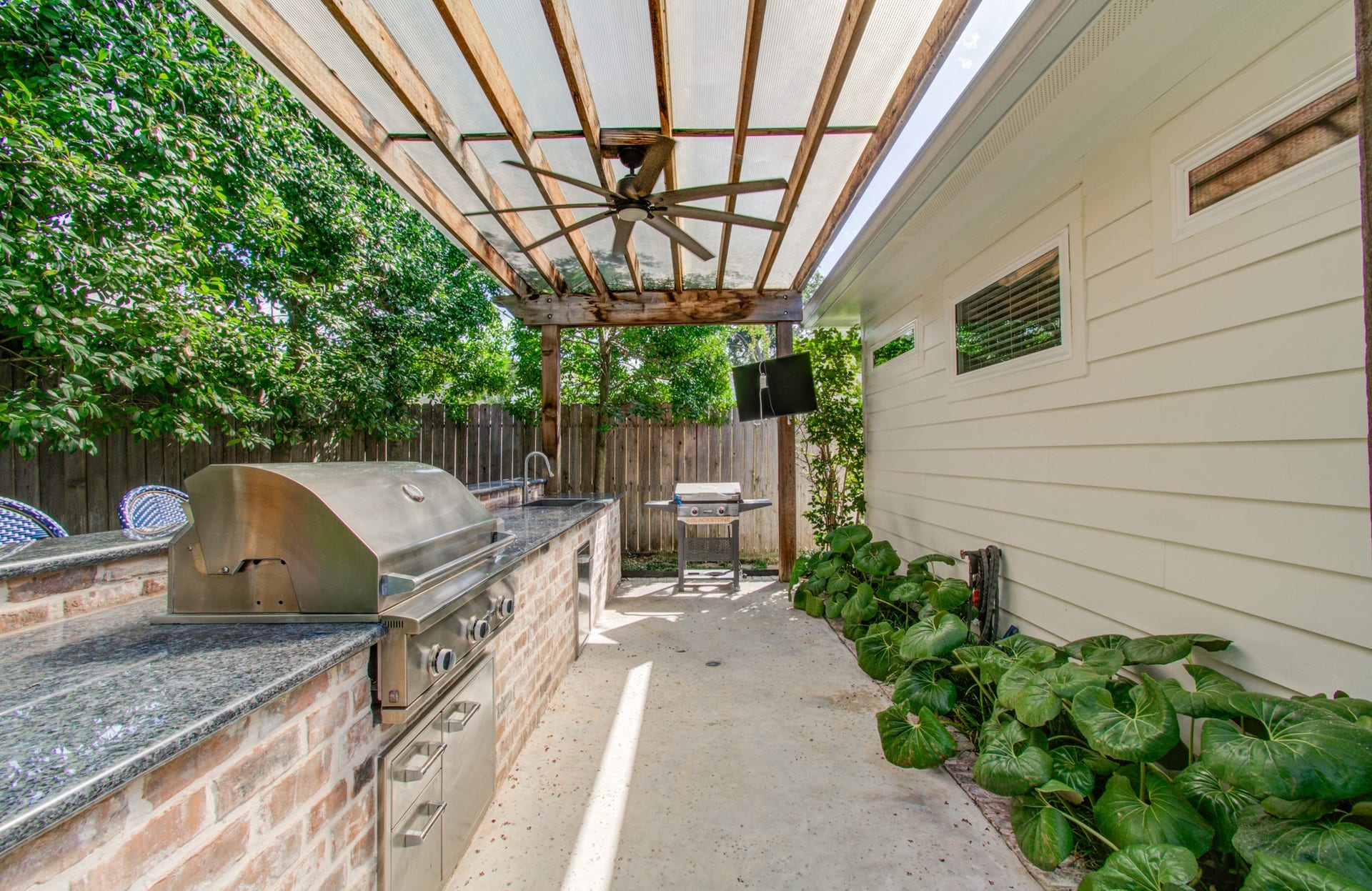 Experience outdoor cooking at its finest with this stylish covered patio featuring a sleek built-in grill, ample counter space, and lush greenery for a perfect backyard retreat.