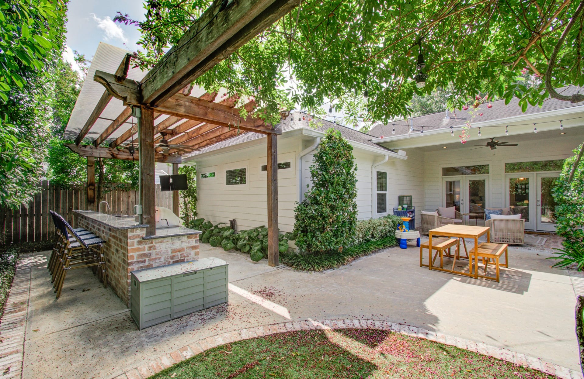 Charming backyard oasis featuring a covered patio, outdoor kitchen with bar seating, and lush landscaping, perfect for entertaining and relaxation.