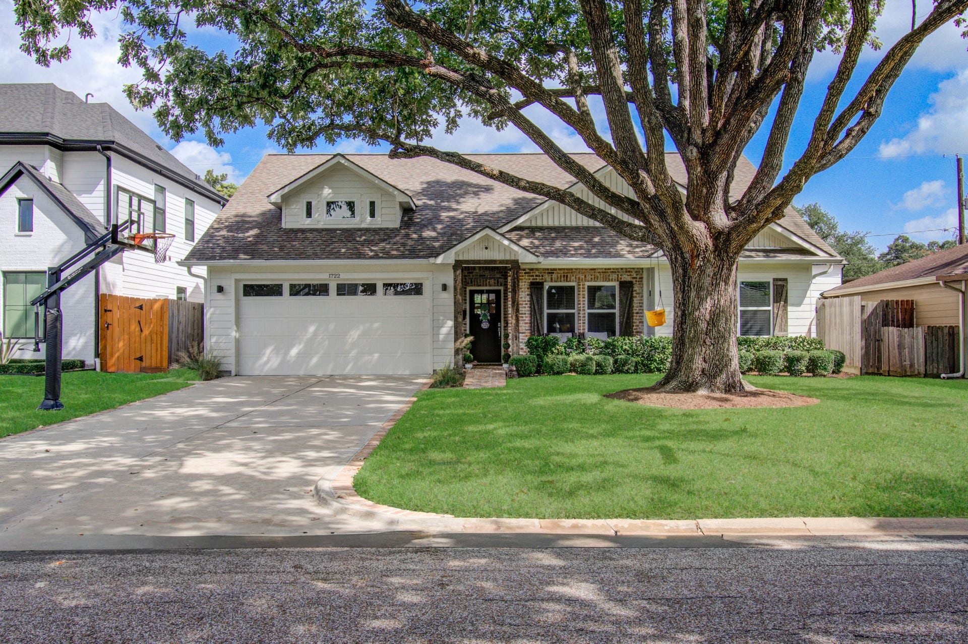 Charming single-story home with a welcoming facade, featuring a spacious driveway, lush green lawn, and a mature shade tree in the front yard.