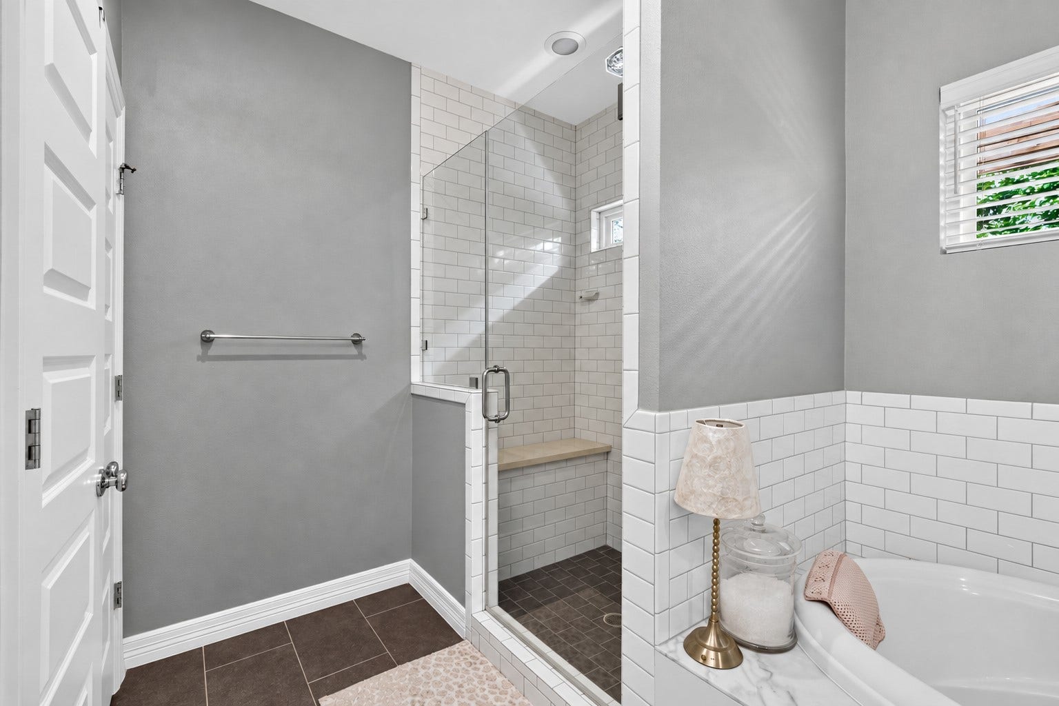 Spacious walk-in shower with subway tile, a cozy bench.