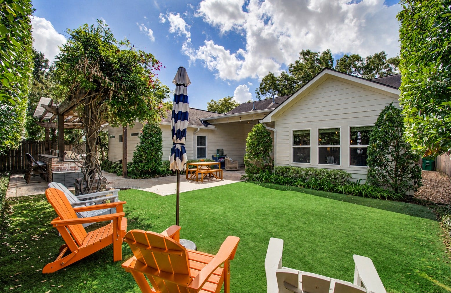 Charming backyard oasis featuring a lush artificial lawn, and a stylish pergola with a cozy seating area perfect for relaxation and entertaining.