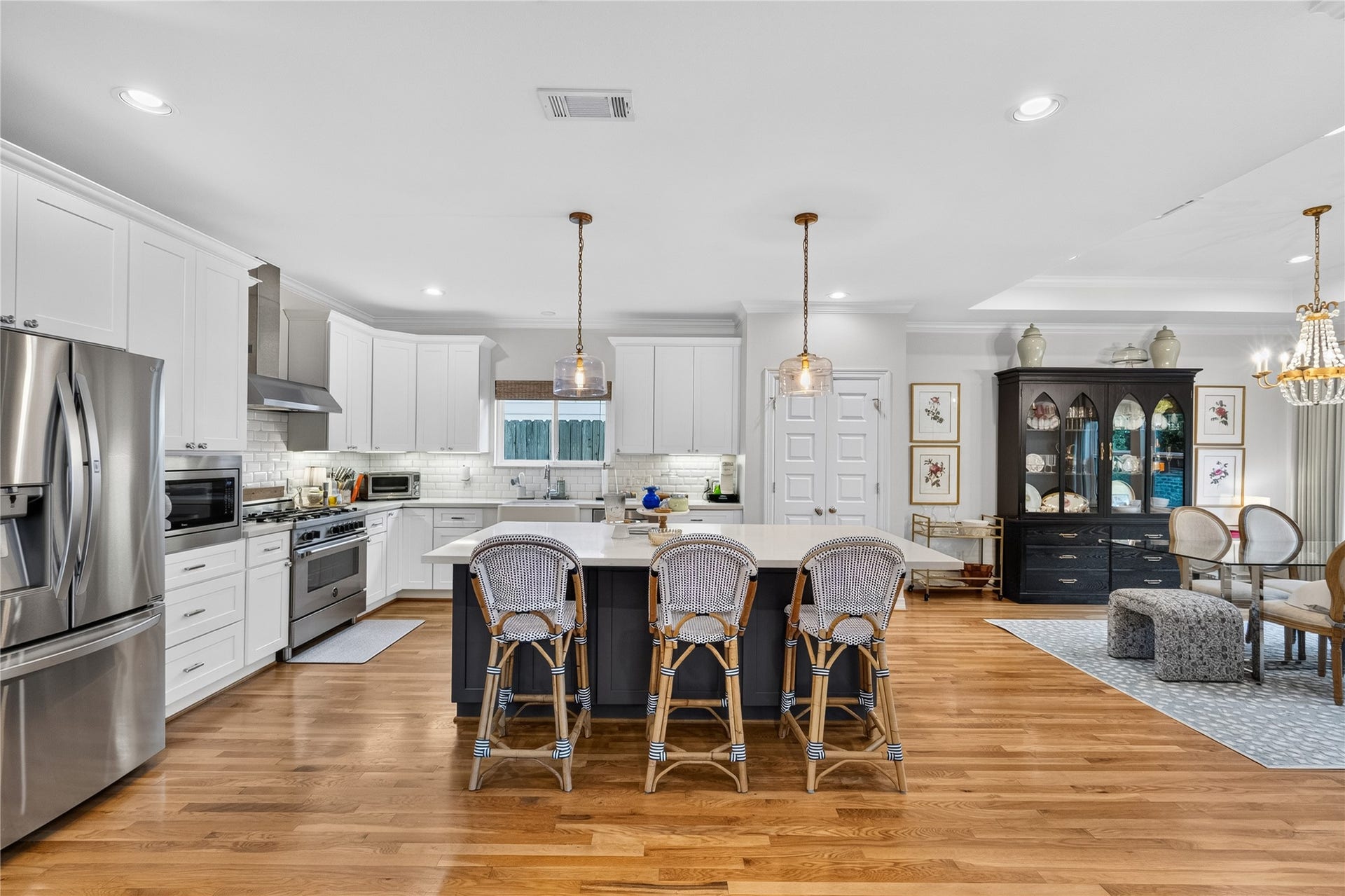 Spacious and elegant kitchen featuring sleek stainless steel appliances, a large island with seating, and white cabinetry, seamlessly flowing into a stylish dining area with a chic lighting.
