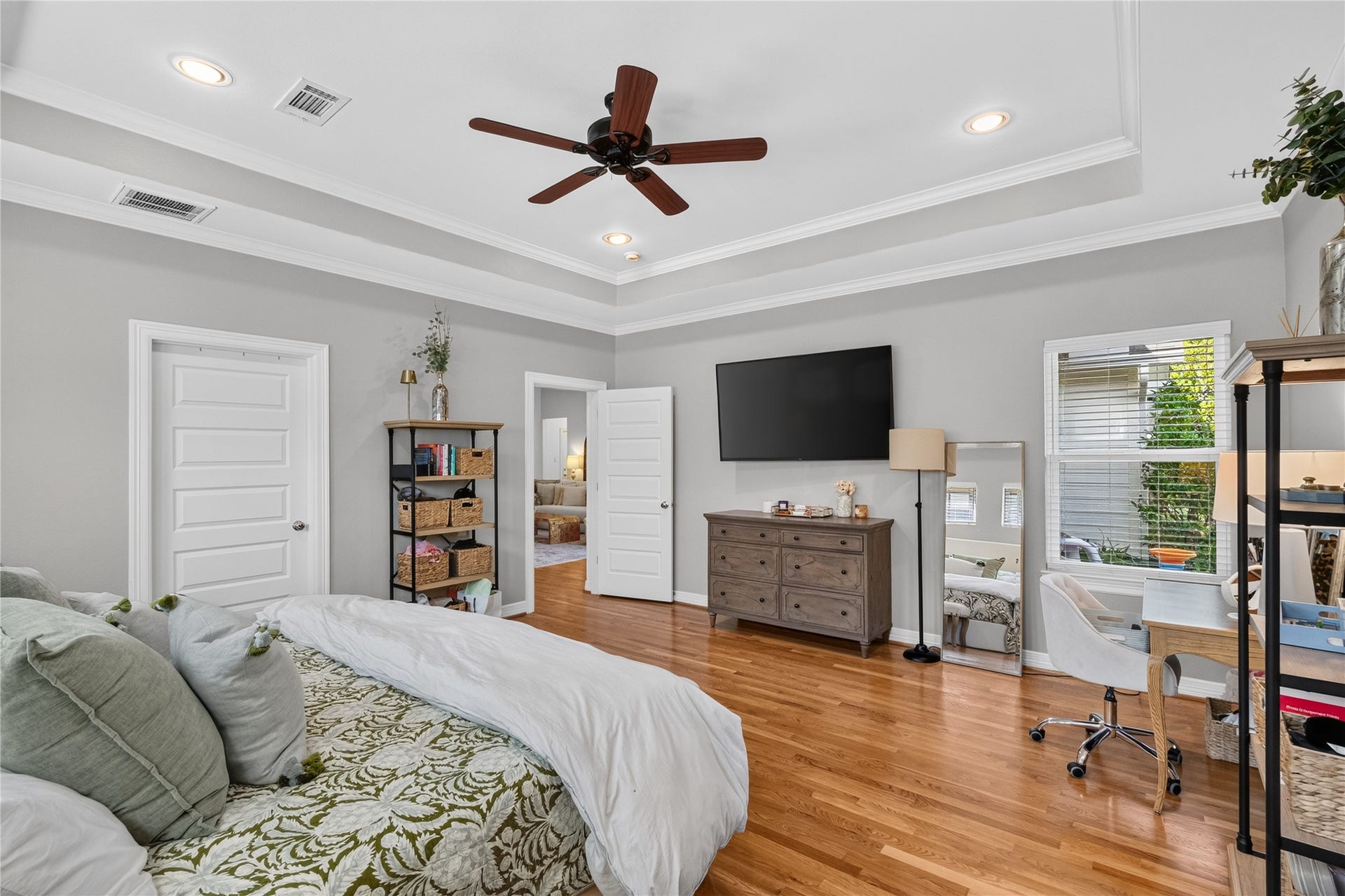 Spacious primary bedroom with hardwood floors, a tray ceiling, and abundant natural light.