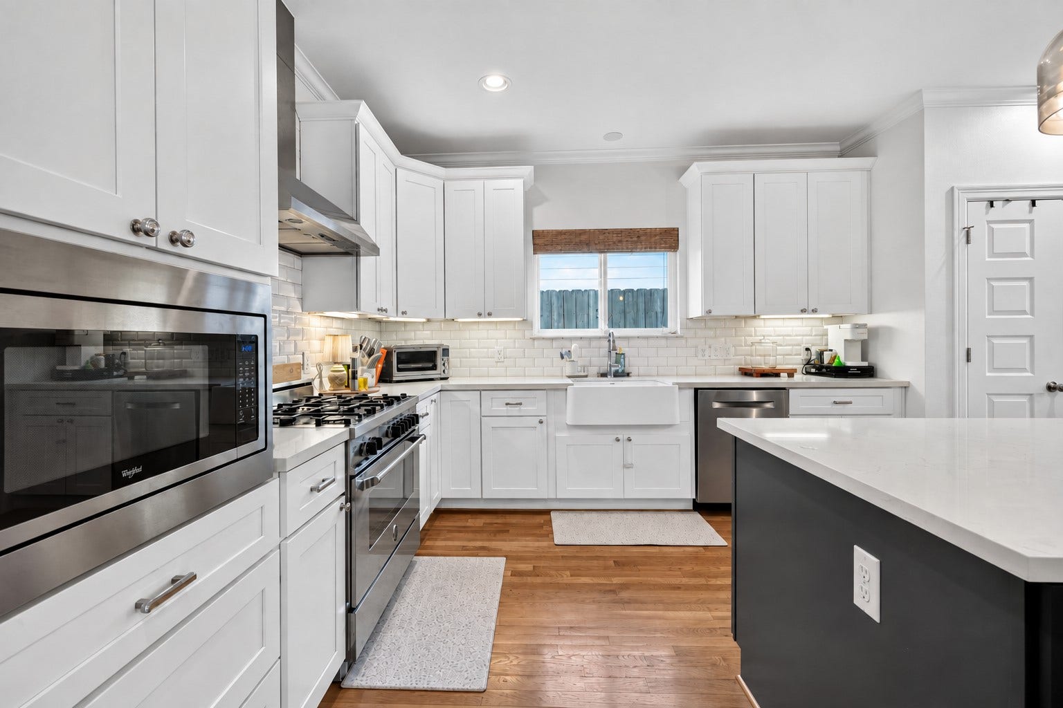 Sleek kitchen with stainless steel appliances, white shaker cabinets, and a farmhouse sink, complemented by a subway tile backsplash and spacious island.