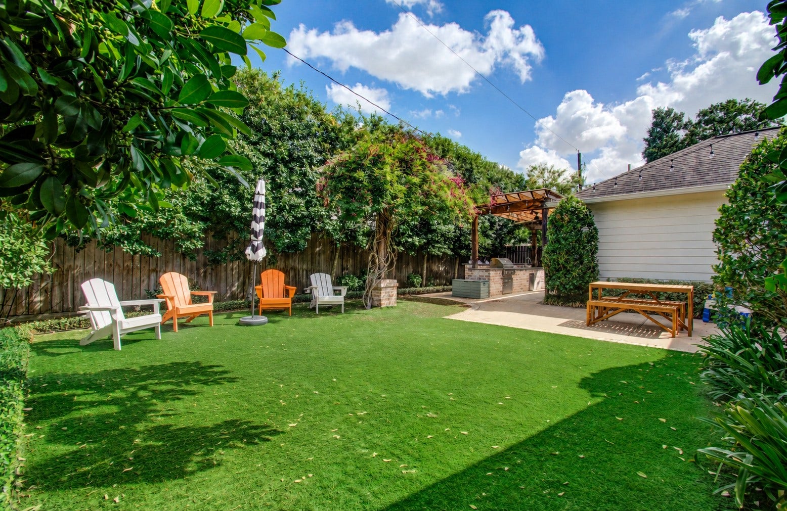 Charming backyard oasis featuring a lush lawn and cozy pergola with an outdoor kitchen, perfect for entertaining and relaxation.