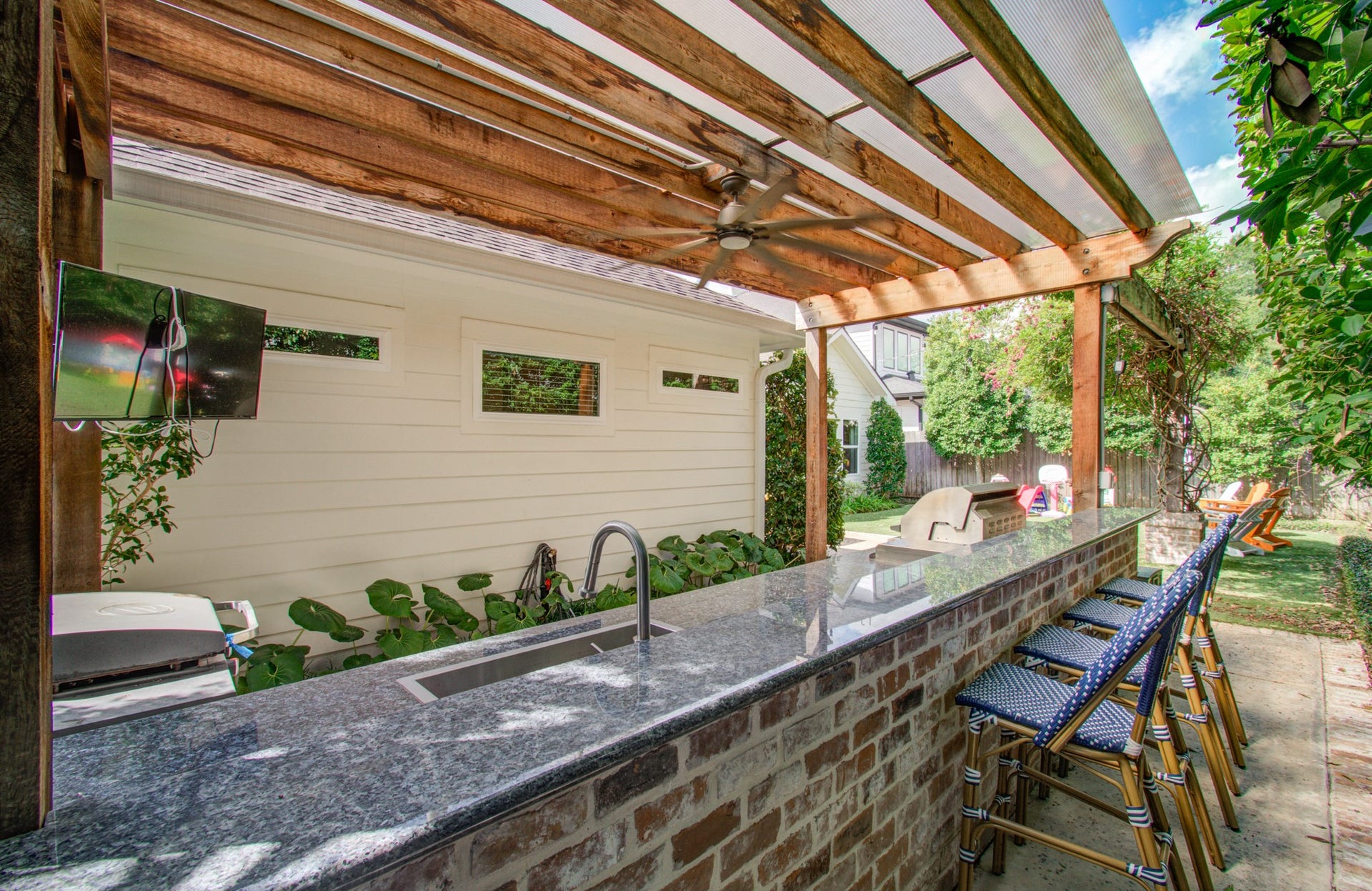 Charming outdoor bar area with a sleek granite countertop, brick base, and a wooden pergola, perfect for entertaining with ample seating and a built-in grill.