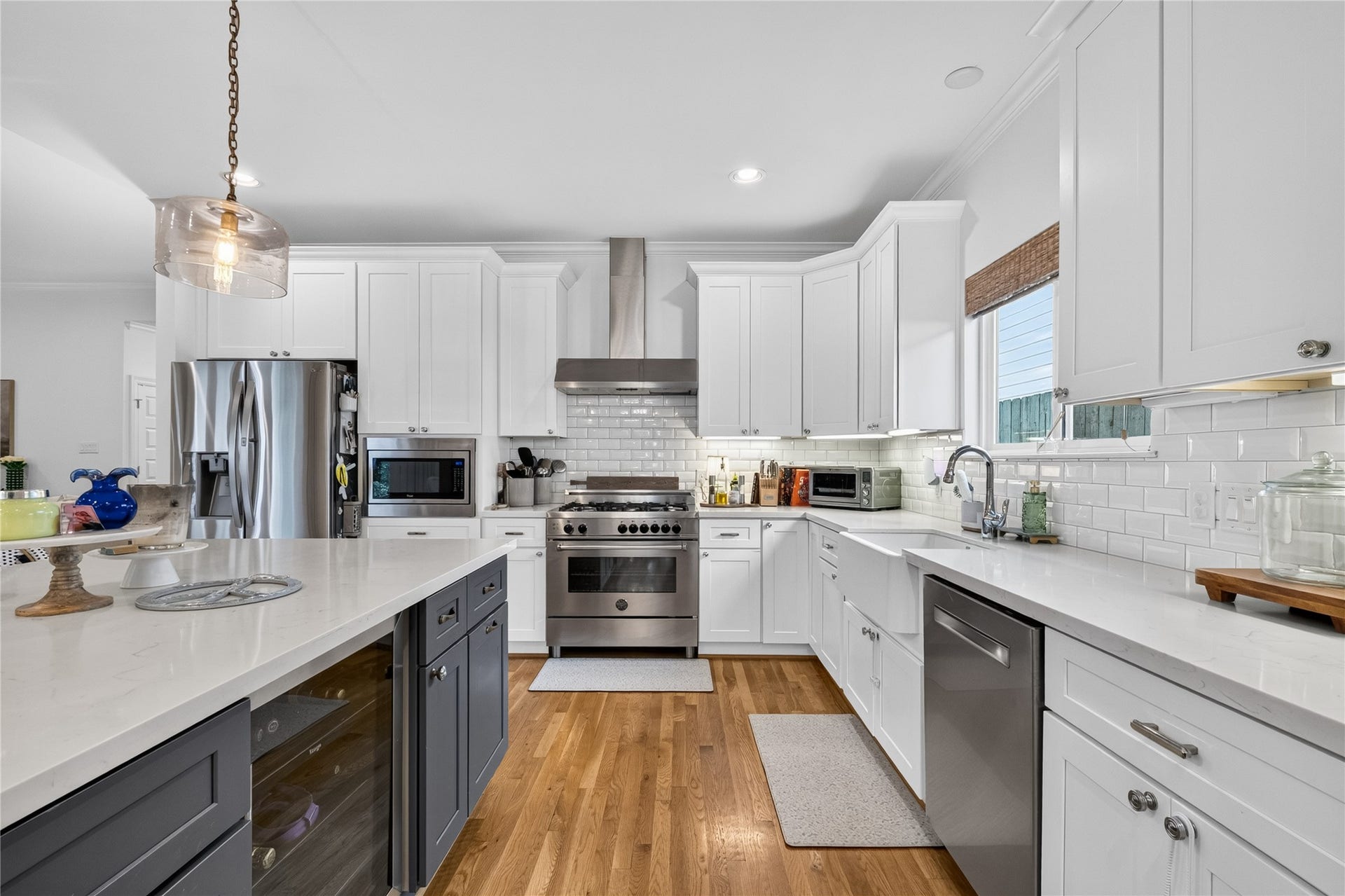 Modern kitchen featuring sleek stainless steel appliances, elegant white cabinetry, and a spacious island with pendant lighting, all set on warm hardwood floors.