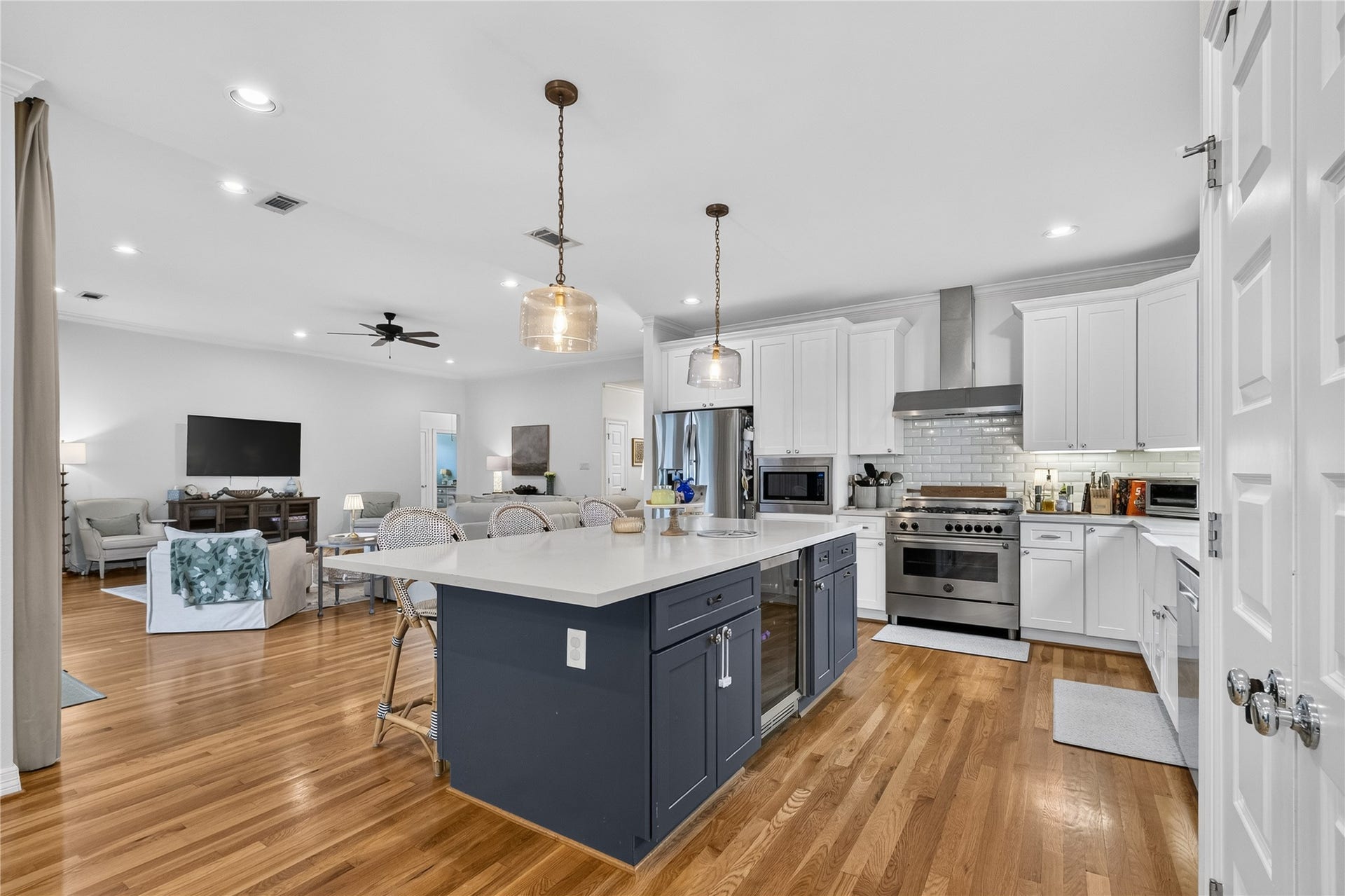 Spacious open-concept kitchen and living area featuring sleek white cabinetry, a large central island with seating, modern stainless steel appliances, and warm hardwood flooring, seamlessly flowing into a cozy living space with ample natural light.