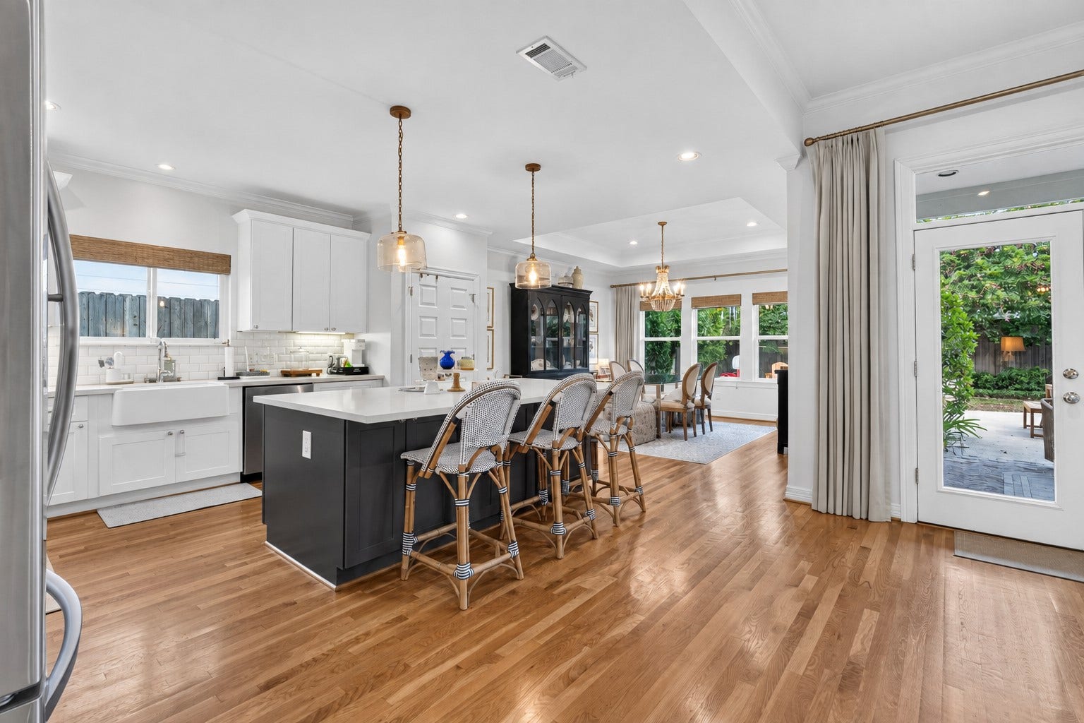 Spacious open-concept kitchen and dining area featuring elegant pendant lighting, a large island with seating, and seamless access to the outdoor patio through French doors.