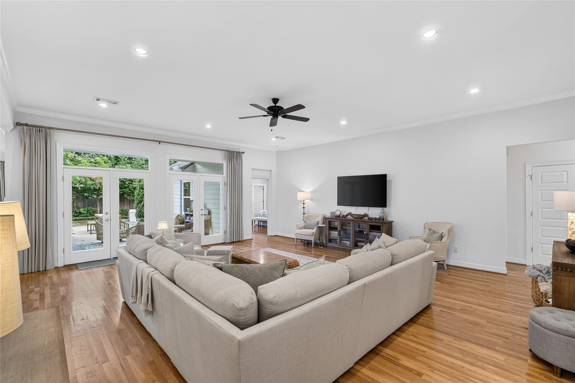 Spacious living room with hardwood floors, a cozy sectional sofa, and abundant natural light from large windows and glass doors leading to the patio.