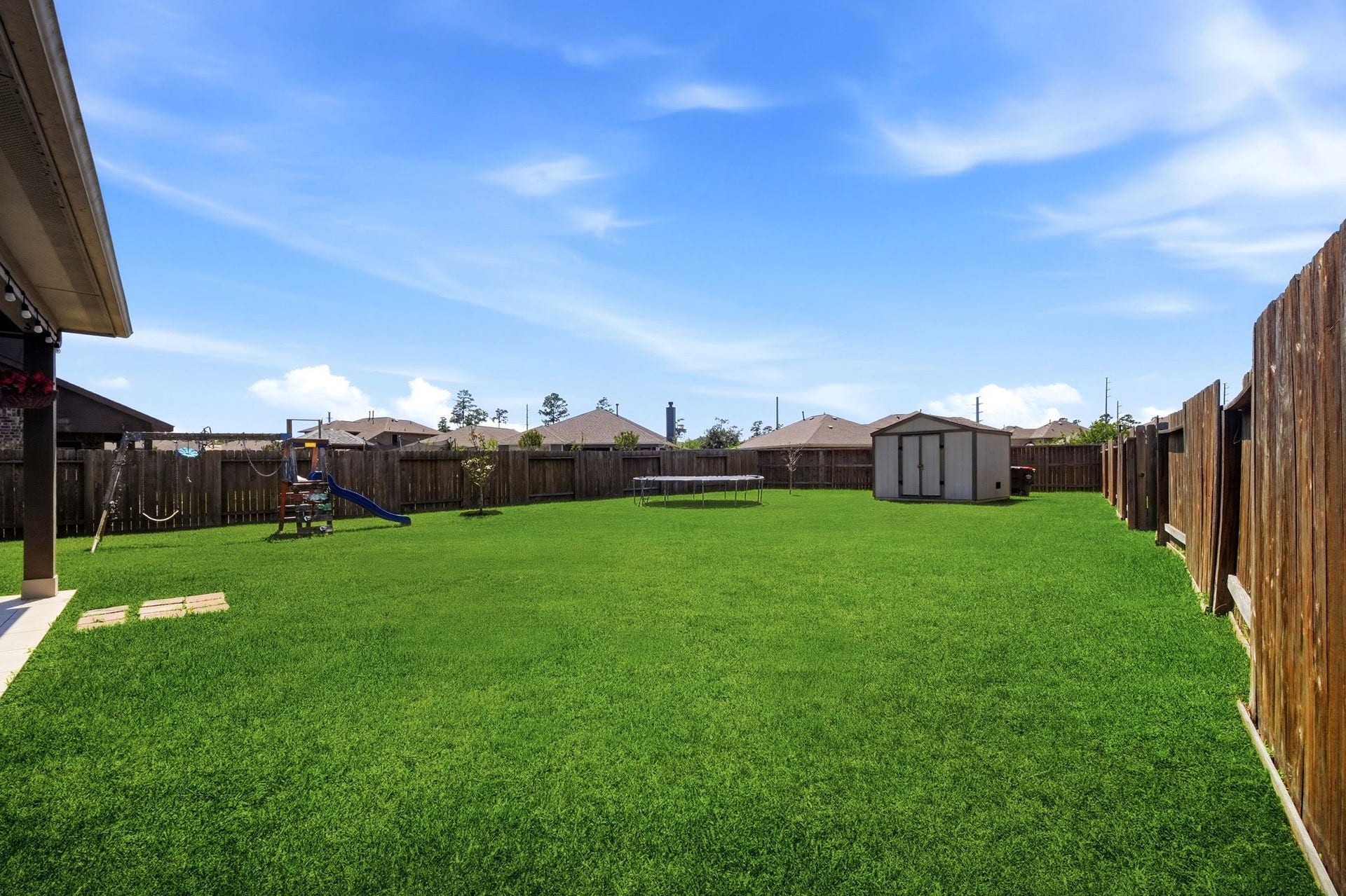 21639 Lexor Drive, Porter, TX 77365 Expansive backyard with lush green lawn, perfect for outdoor activities, featuring a playground, trampoline, and a spacious storage shed.