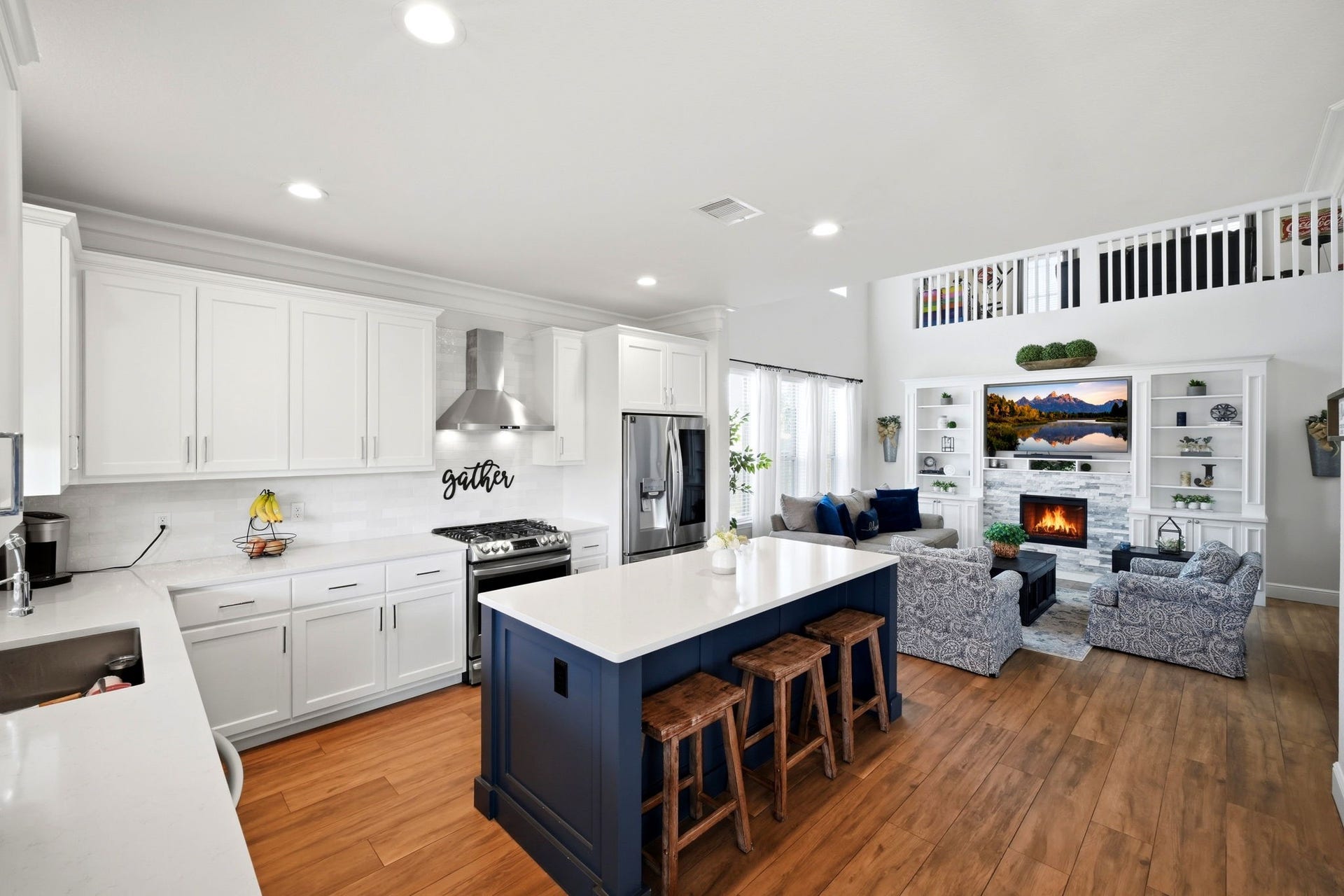 21639 Lexor Drive, Porter, TX 77365 Experience open-concept living with this stylish kitchen and cozy living area, featuring sleek white cabinetry, a central island with seating, and a warm fireplace flanked by built-in shelves.