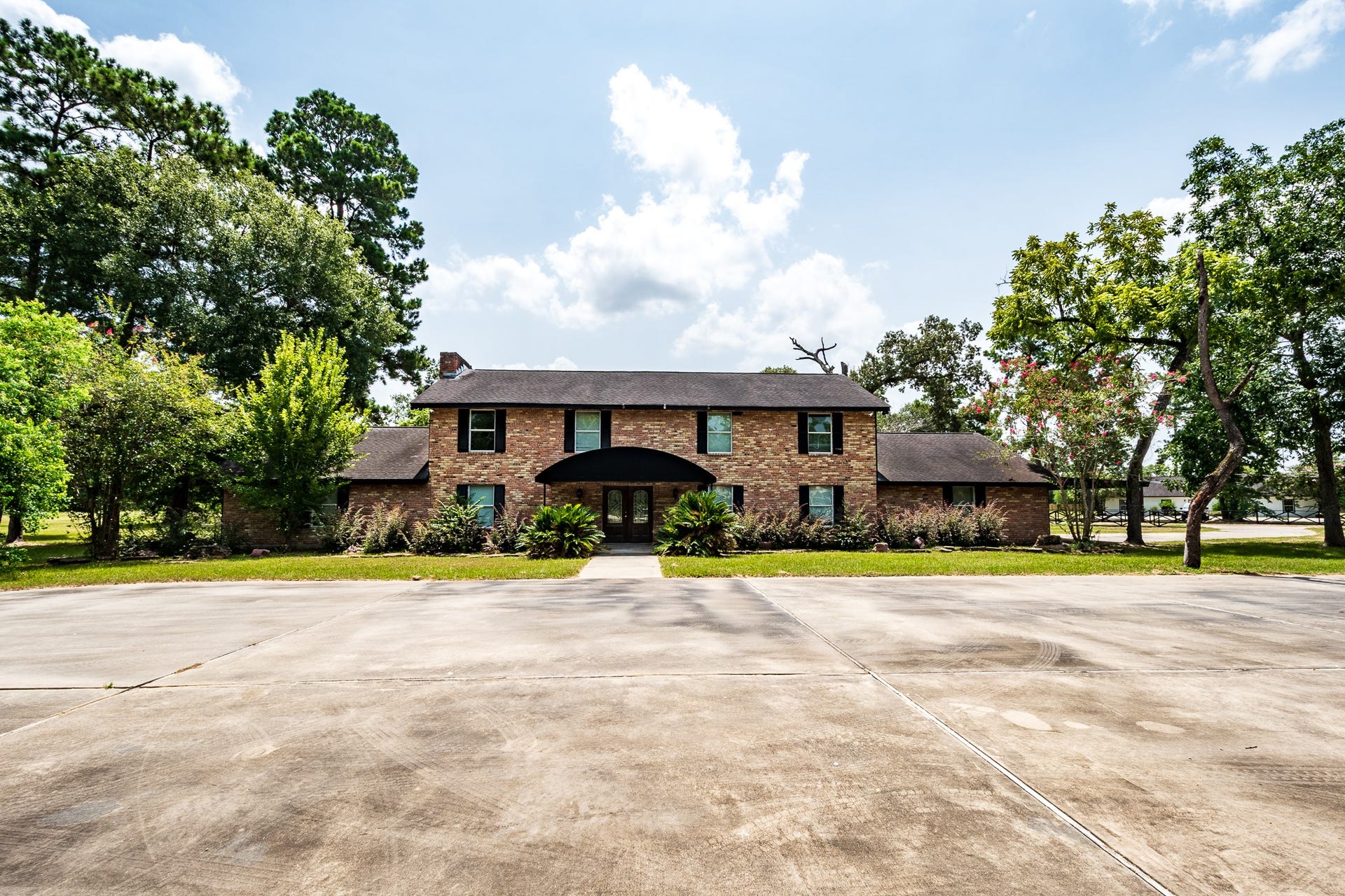 16111 Porter Lane, Porter, TX 77365 Stately two-story brick home surrounded by mature trees, featuring a spacious driveway and a welcoming entrance.