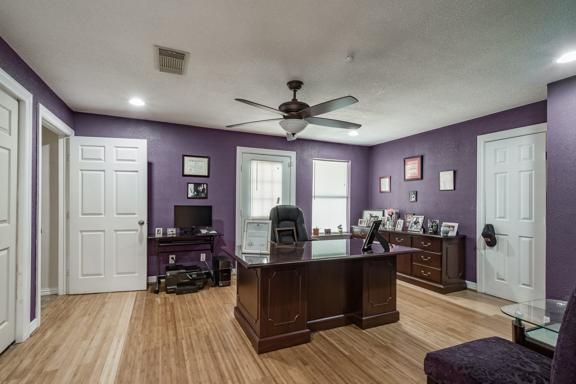 16111 Porter Lane, Porter, TX 77365 Home office features rich purple walls, elegant wood flooring, and ample natural light. The room is equipped with a large executive desk, shelving for storage, and a ceiling fan for comfort.