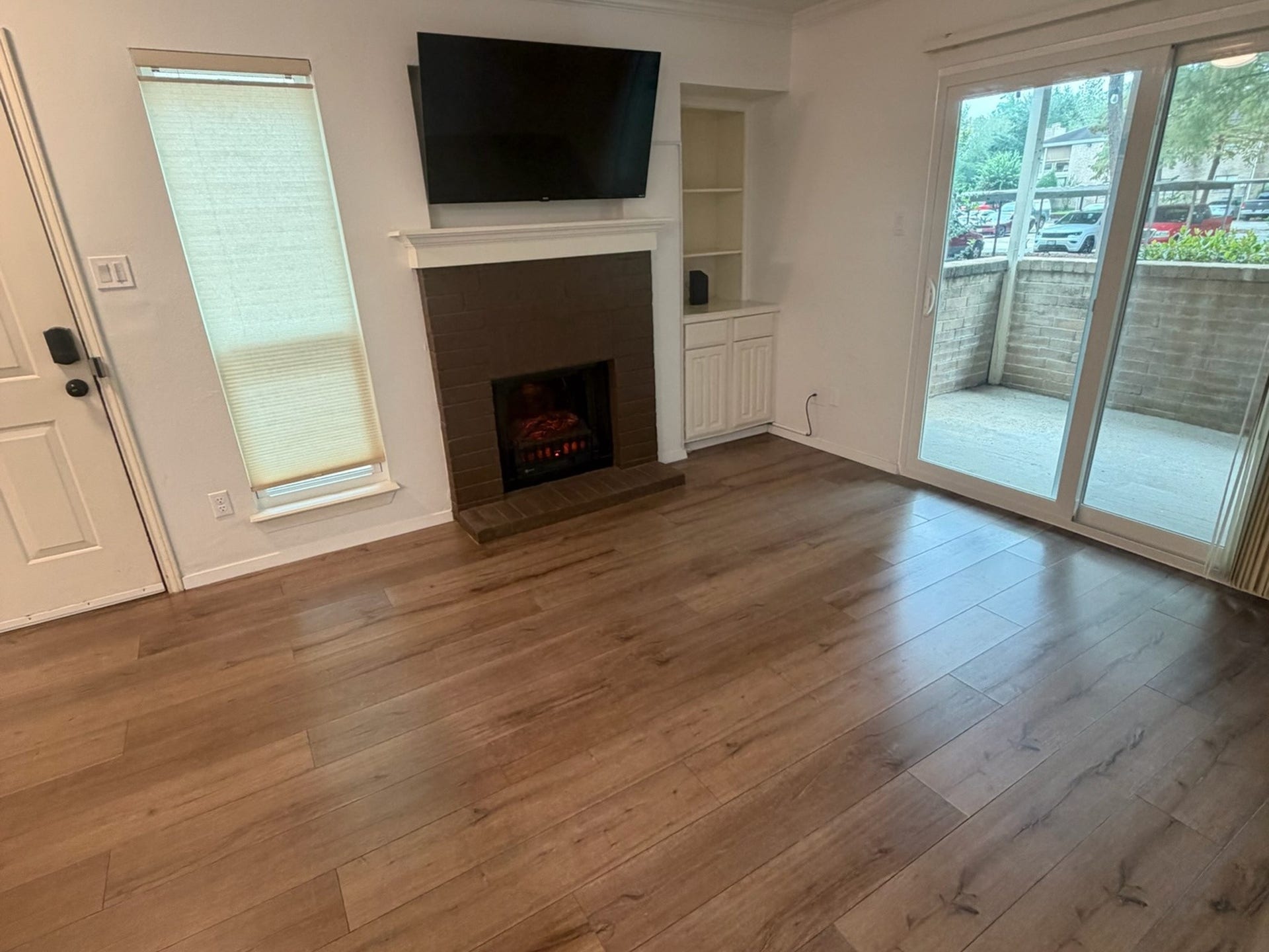 3500 Tangle Brush Drive, #65, The Woodlands, TX 77381 New electric fireplace with built-in storage, crown molding, wood-look floors, and a 2026 patio door opening to the private covered patio.