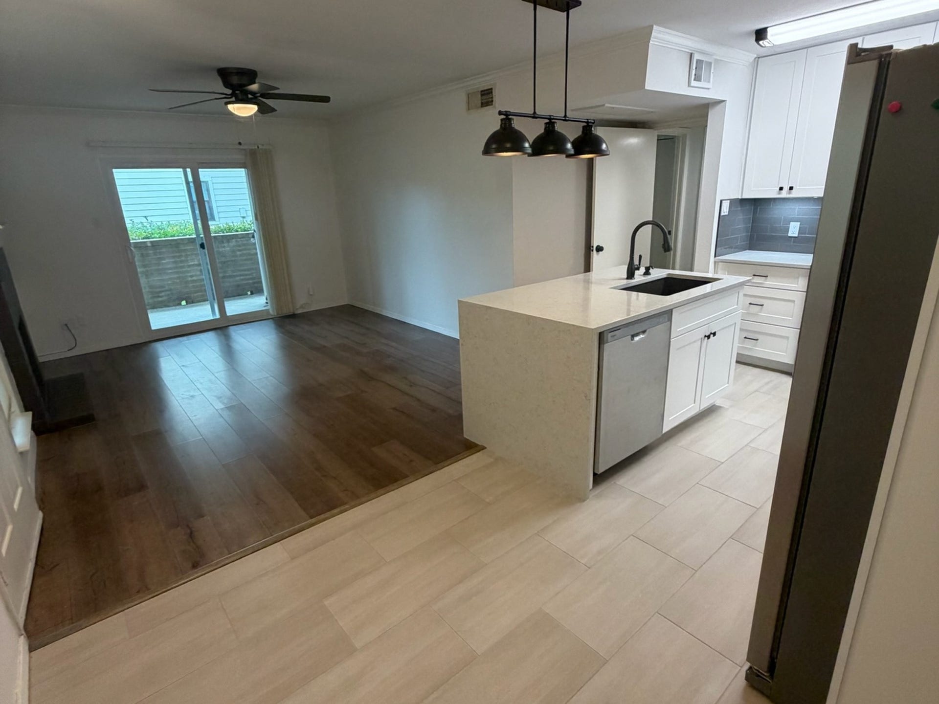 3500 Tangle Brush Drive, #65, The Woodlands, TX 77381 Open-concept layout connects the updated kitchen and living area, featuring contrasting flooring, a waterfall-edge island with sink and dishwasher, modern pendant lighting, and sliding glass doors that extend the living space to the private patio.