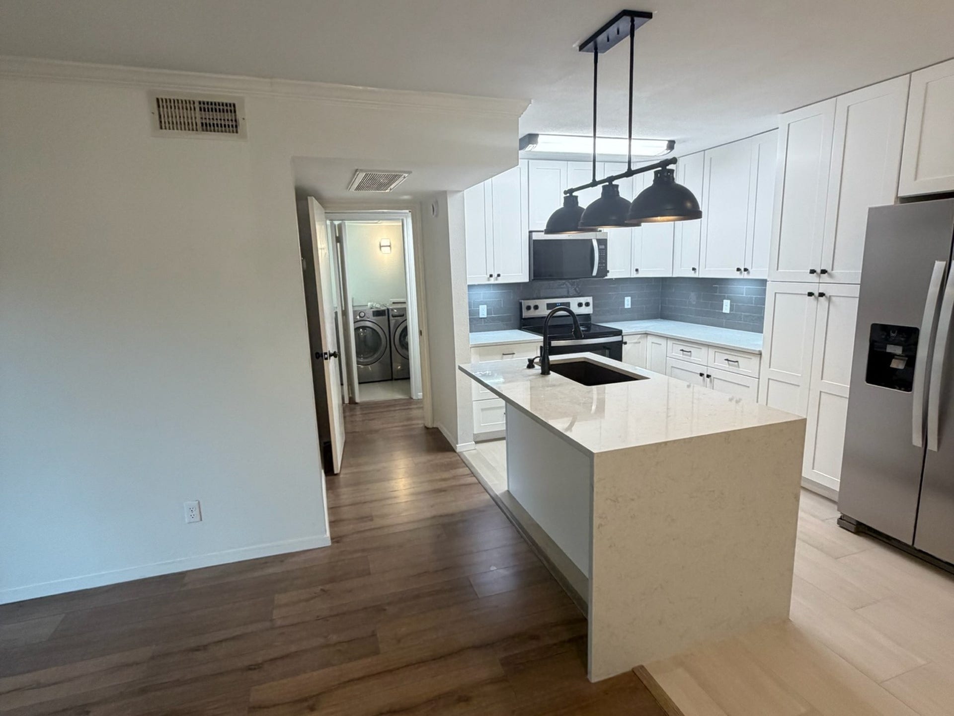 3500 Tangle Brush Drive, #65, The Woodlands, TX 77381 Rebuilt kitchen with new white cabinetry, quartz counters, subway-tile backsplash, under-cabinet lighting, waterfall-edge island, and a new stainless Whirlpool package: refrigerator, range, over-the-range microwave, and dishwasher.