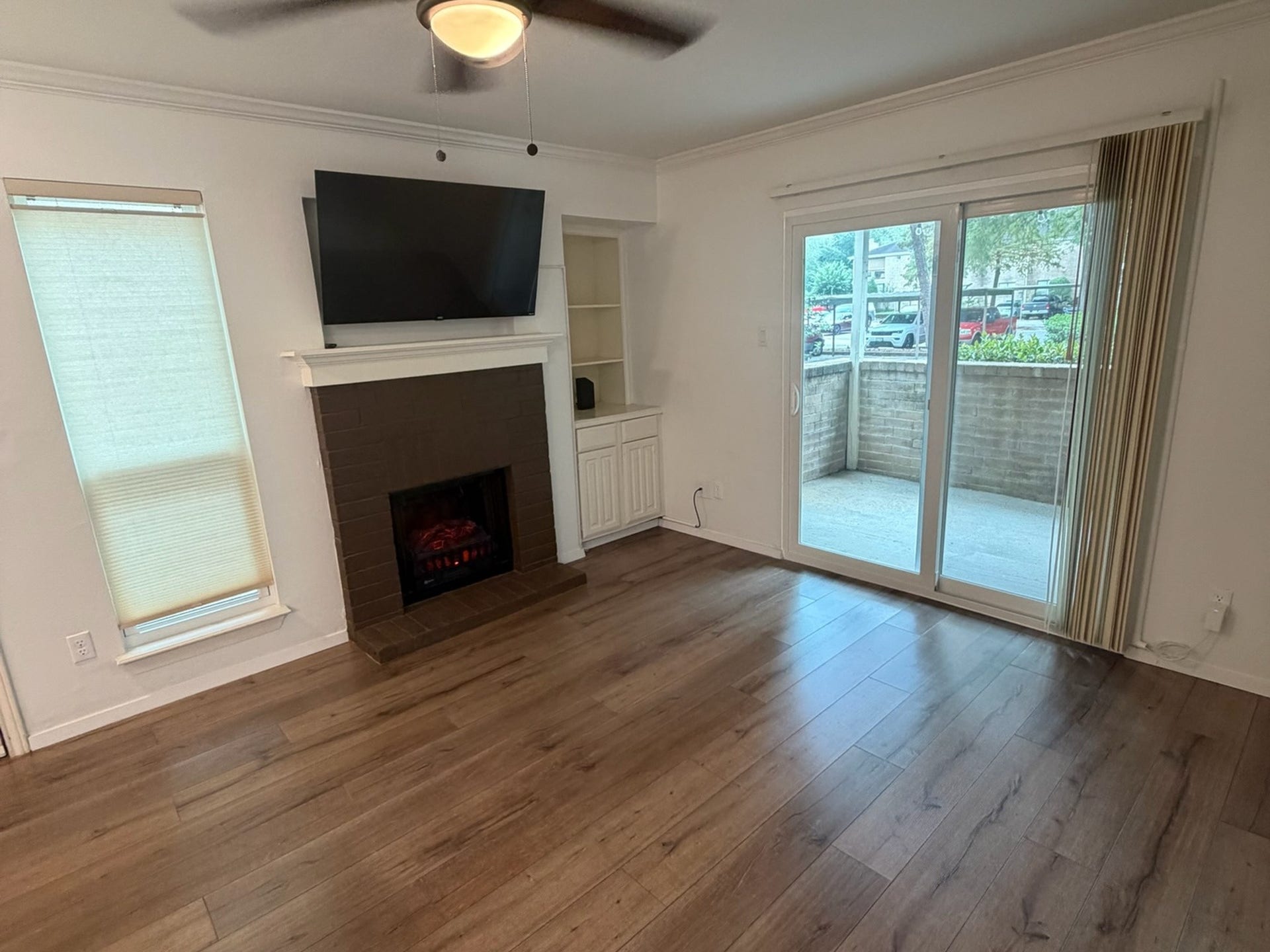 3500 Tangle Brush Drive, #65, The Woodlands, TX 77381 Comfortable living area features a cozy fireplace with built-in shelving and cabinetry, crown molding, wood-look flooring, and sliding glass doors that fill the space with natural light and open to the private patio.