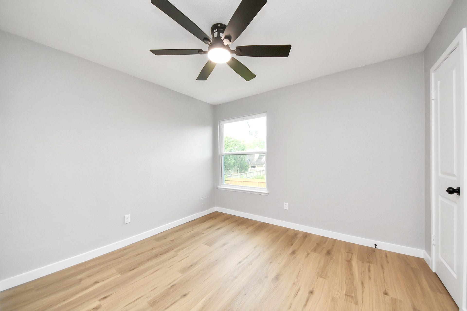 3234 Pebble Lake Drive, Sugar Land, TX 77479 Bedroom 3 - a bright, minimalist room with light hardwood flooring, neutral gray walls, and a ceiling fan. The window offers natural light and a view of the backyard, creating an inviting space.