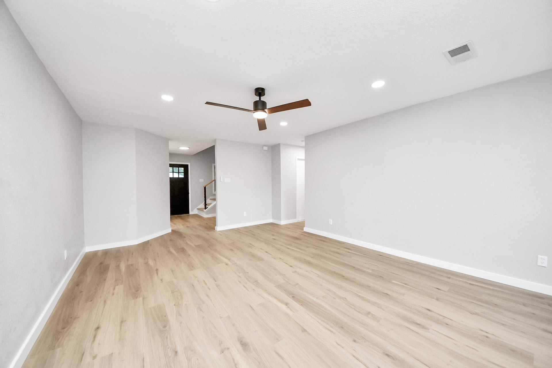 3234 Pebble Lake Drive, Sugar Land, TX 77479 This room features a spacious, open layout with light wood flooring, neutral gray walls, recessed lighting, and a modern ceiling fan. It leads to a staircase and entryway, ideal for a contemporary living space.
