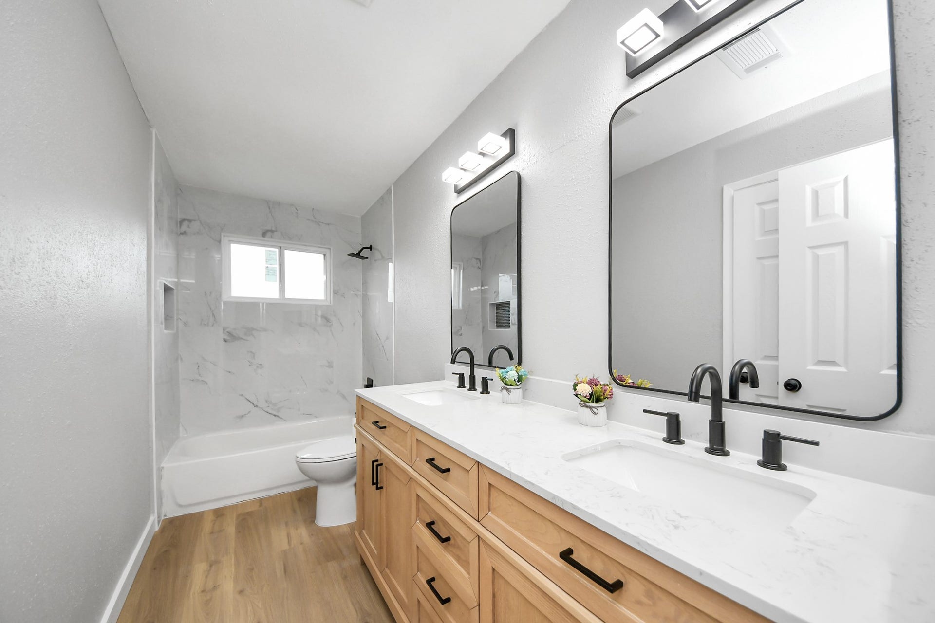3234 Pebble Lake Drive, Sugar Land, TX 77479 This bathroom features a modern design with a double vanity, sleek black fixtures, and a large mirror. The space includes a bathtub with elegant marble-style tiling and natural wood flooring, creating a bright and inviting atmosphere.