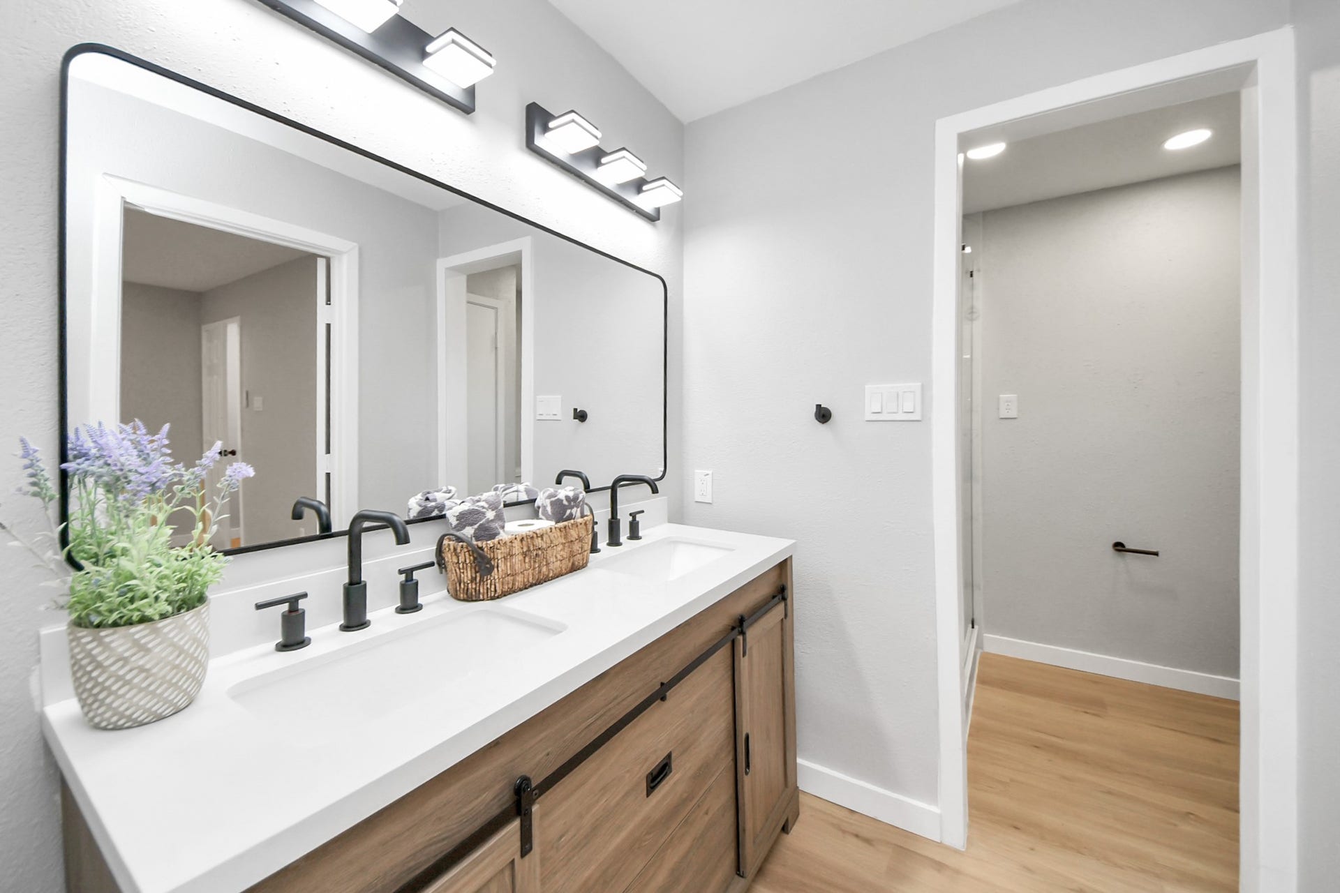 3234 Pebble Lake Drive, Sugar Land, TX 77479 This modern bathroom features a double vanity with sleek black fixtures, a large mirror, and stylish lighting. The space is enhanced by a light wood floor and neutral walls, creating a clean and inviting atmosphere.