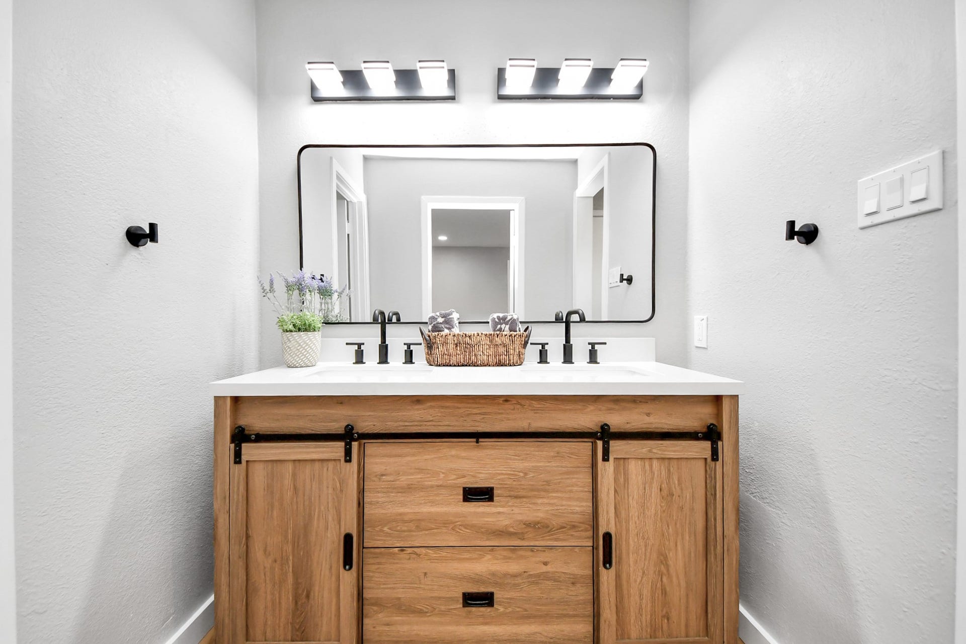 3234 Pebble Lake Drive, Sugar Land, TX 77479 Primary bathroom features a modern vanity with a wooden cabinet and sliding barn doors, a sleek rectangular mirror, and contemporary lighting. The decor is minimalistic with a small plant and basket for added charm.