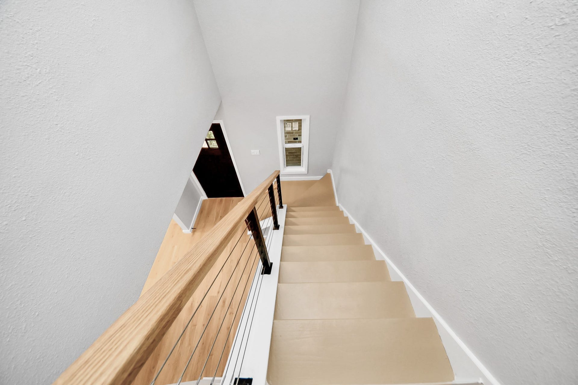 3234 Pebble Lake Drive, Sugar Land, TX 77479 Modern staircase with light beige steps and a sleek wooden handrail, leading down to a bright hallway with a small window. The minimalist design enhances the spacious feel.