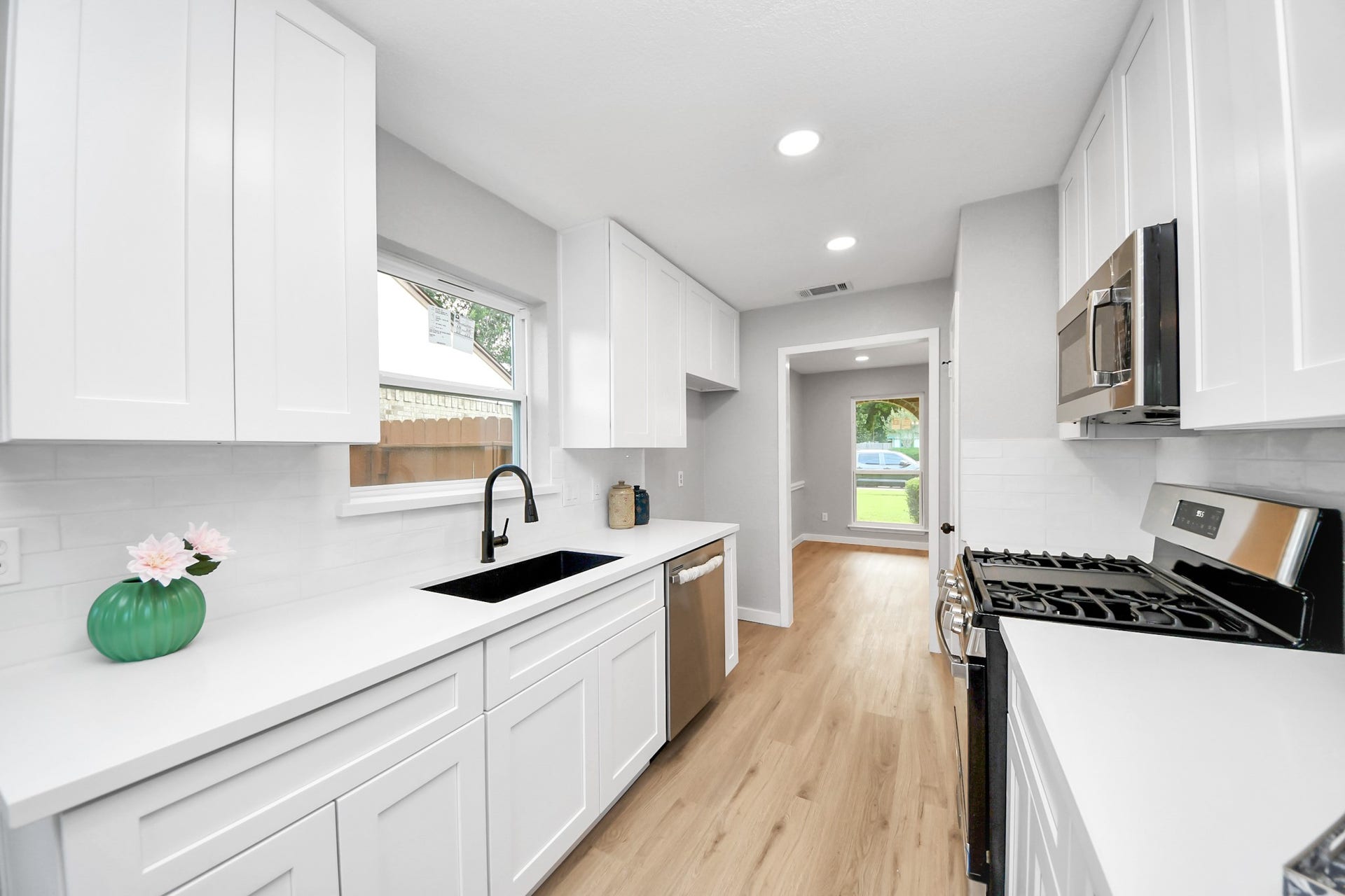3234 Pebble Lake Drive, Sugar Land, TX 77479 This kitchen features a sleek, modern design with white cabinetry, stainless steel appliances, and a black sink. It has a bright and airy feel, with ample natural light from the window and recessed lighting. The light wood flooring adds warmth to the space.