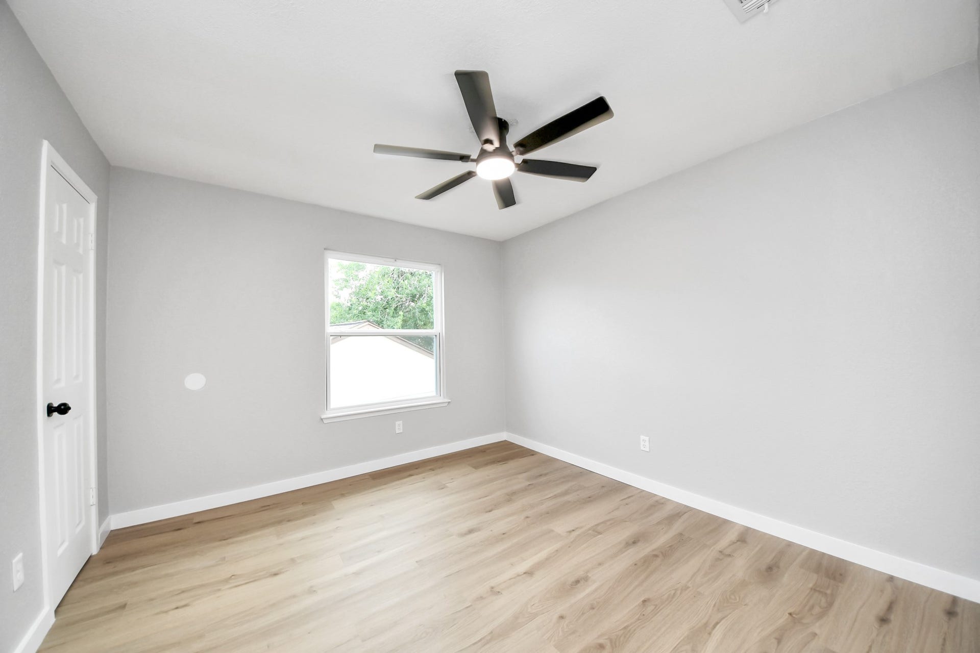 3234 Pebble Lake Drive, Sugar Land, TX 77479 Bedroom 2 - A bright, modern room with light gray walls and wood-look flooring. It features a ceiling fan, a window providing natural light, and a white door.