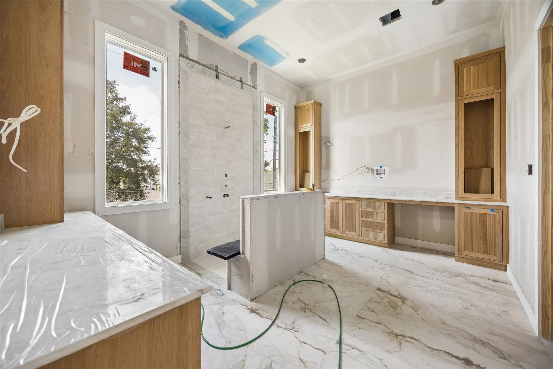 Primary bath takes shape as a true retreat with marble look porcelain flooring, warm custom cabinetry and a spacious walk in shower framed by tall windows for abundant natural light. **Current Construction as of 9/11/26
