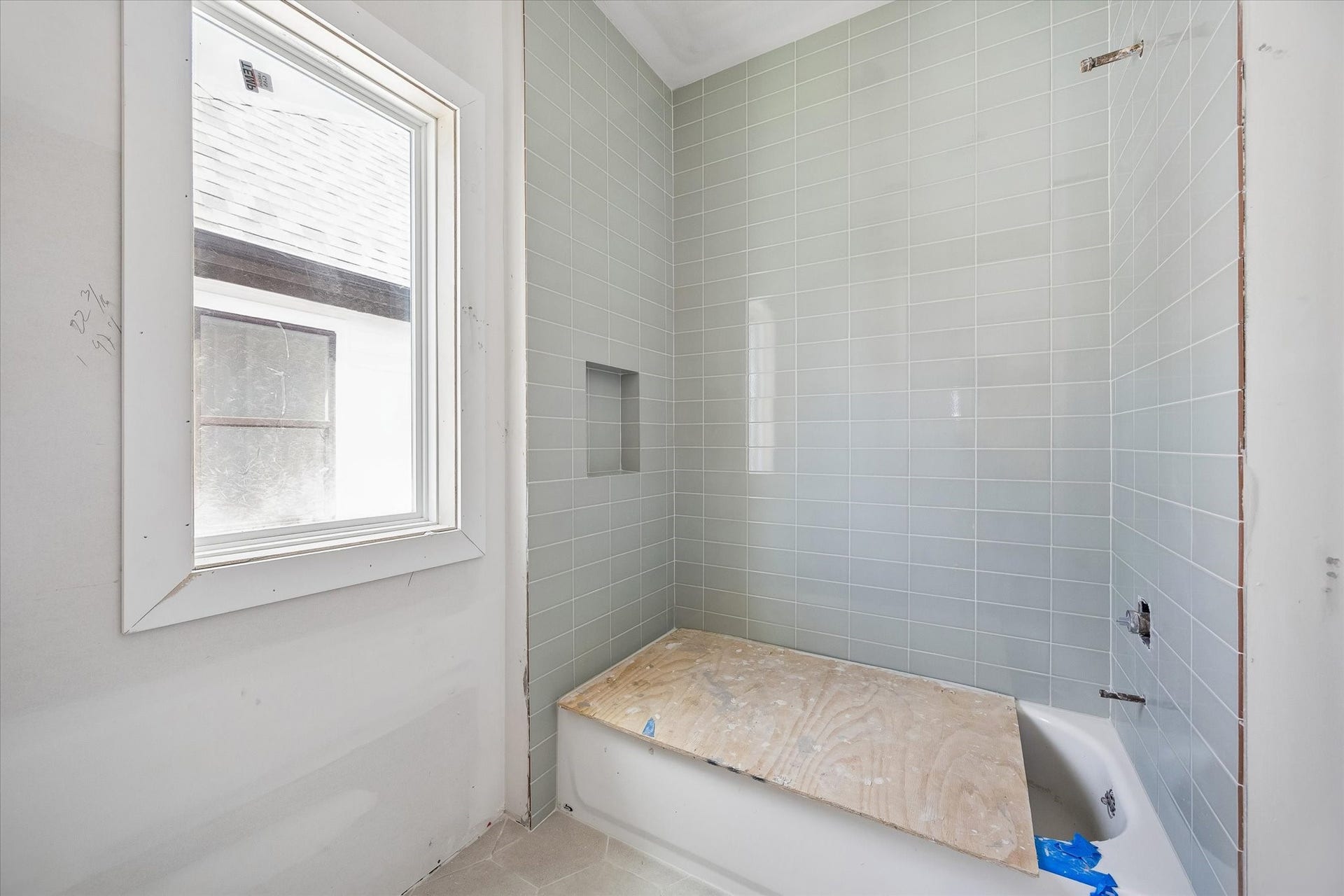 Jack and Jill bath features a tub and shower combination wrapped in soft green tile, with a built in niche for everyday essentials. A nearby window brings natural light into the bathing area. **Current Construction as of 9/11/26