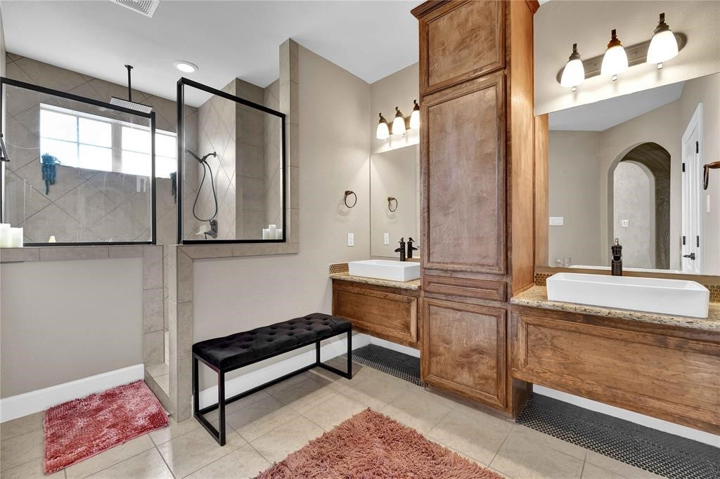 14502 San Pietro Drive, Houston, TX 77070 Luxurious bathroom featuring walk-in shower with modern glass enclosure, dual vessel sinks with elegant fixtures, and warm wood cabinetry for ample storage!