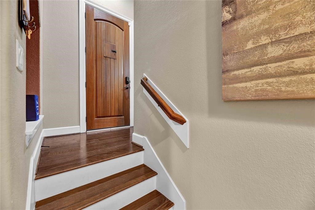 14502 San Pietro Drive, Houston, TX 77070 Warm and inviting staircase leading to a beautifully crafted wooden door, enhanced by elegant hardwood flooring and a stylish handrail.