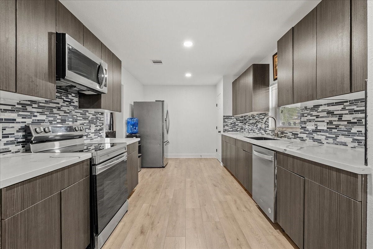5201 Main Street, Santa Fe, TX 77510 The eye-catching mosaic glass tile backsplash adds a touch of texture and personality, beautifully complementing the kitchens black, white, and gray color palette.