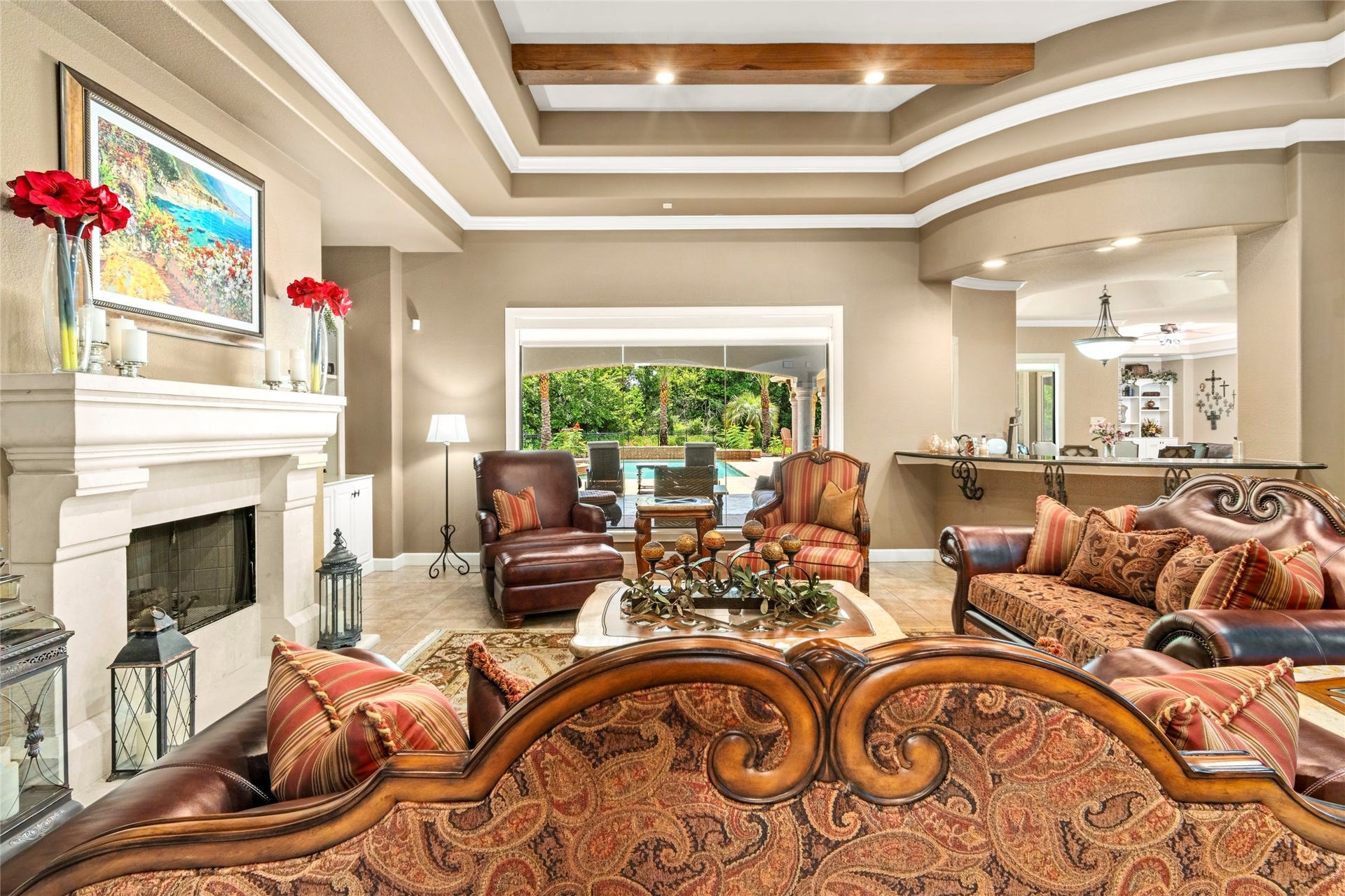 The formal living room has a wall of glass overlooking the lush backyard oasis. One of the five exquisitely detailed fireplaces in this room and a view into the wet bar area which is perfectly situated between the kitchen and family room.