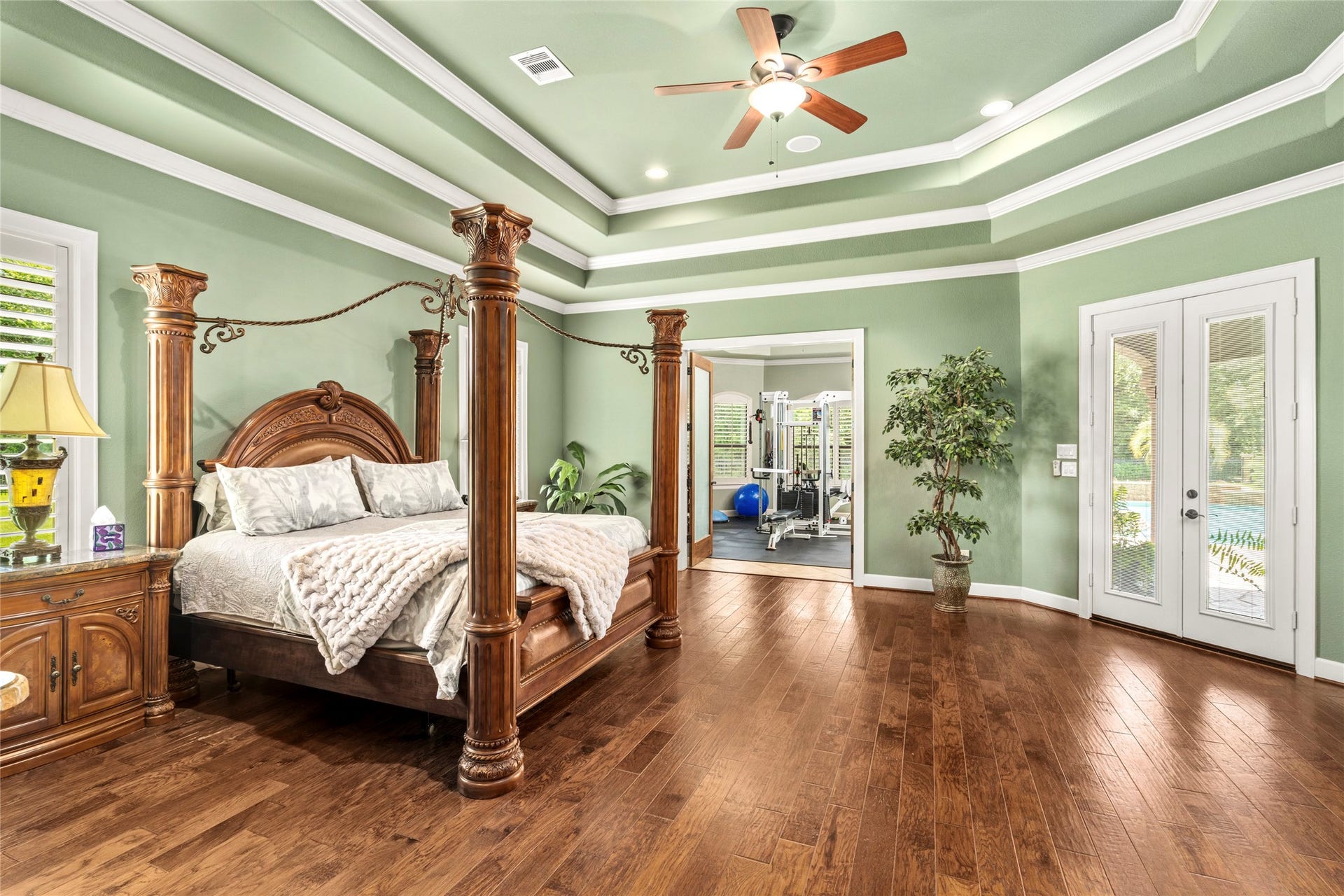 The primary suite features triple tray ceilings and custom wood floors, with double French doors opening to the backyard oasis. Separate doors lead to a versatile flex space currently used as a home gym.